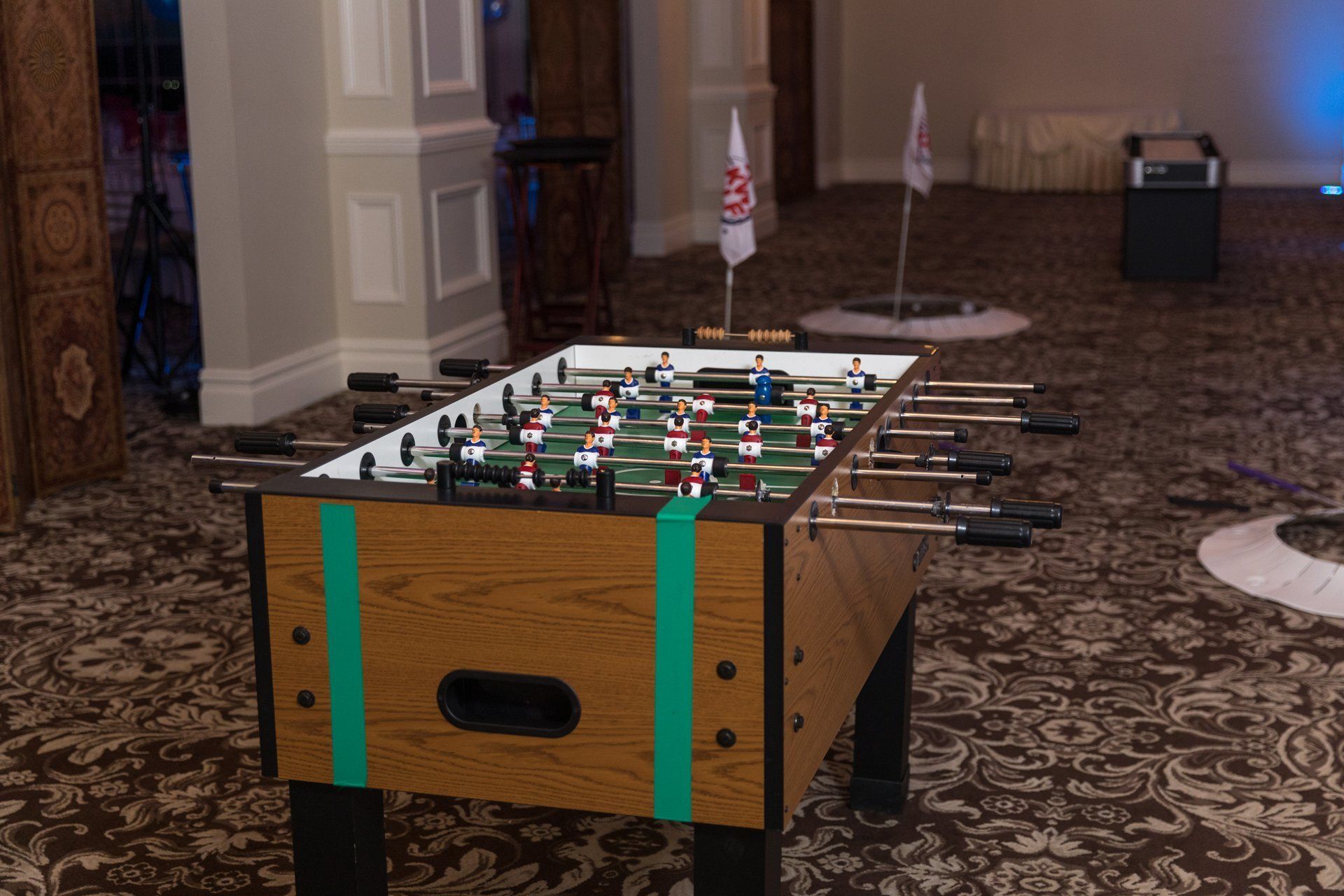Foosball table in a carpeted indoor room, with figures on the playfield and cue sticks beside it