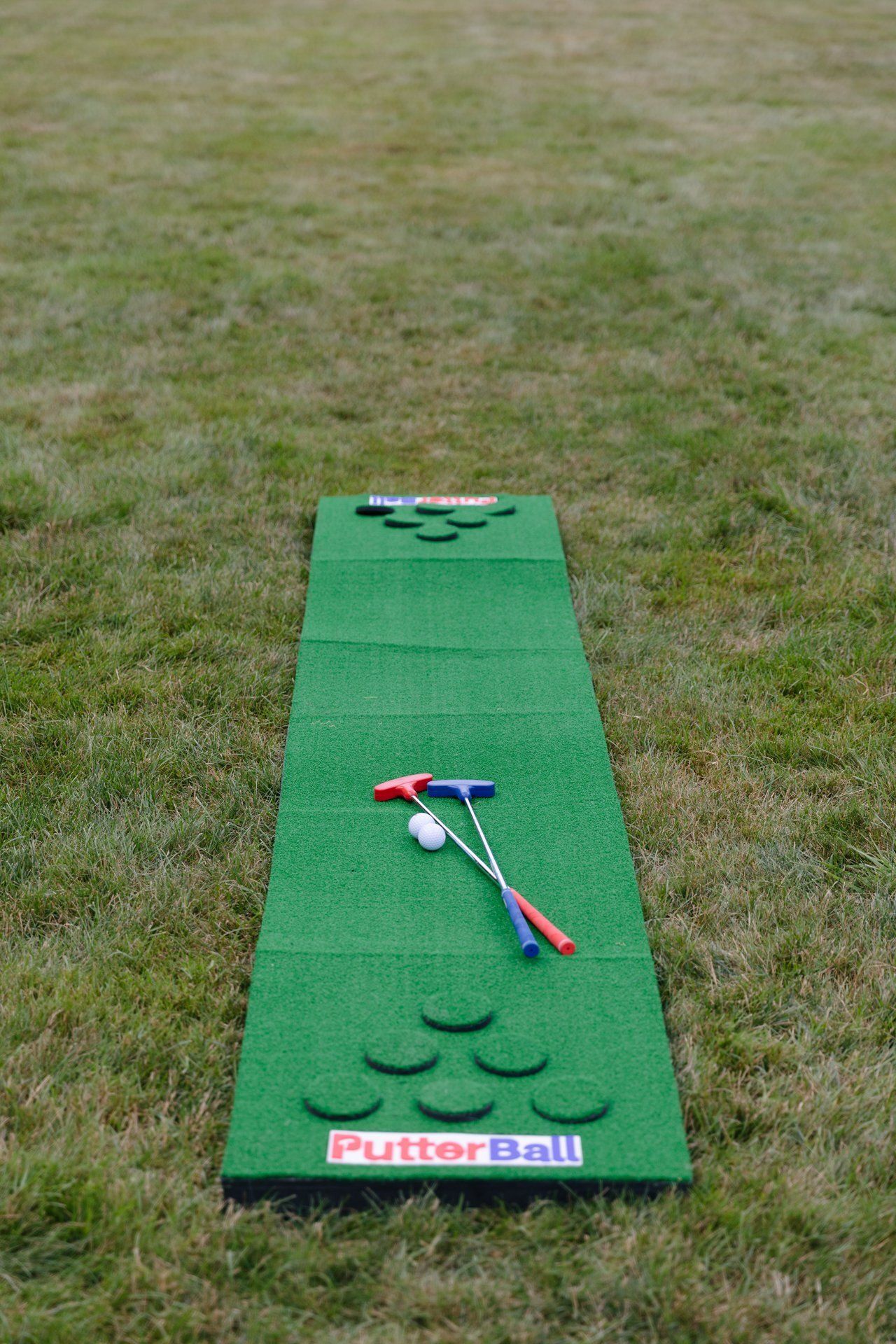 Green putting mat on grass with a putter and golf balls.