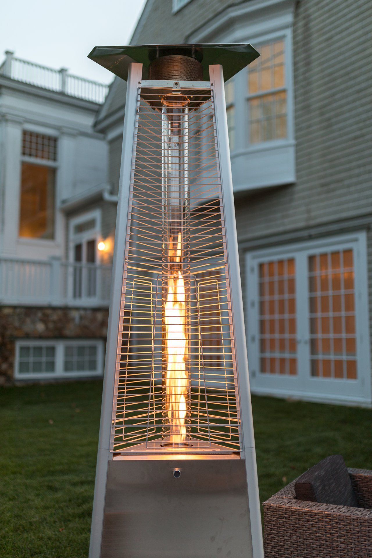 Lit outdoor patio heater glowing in a courtyard beside a house at dusk