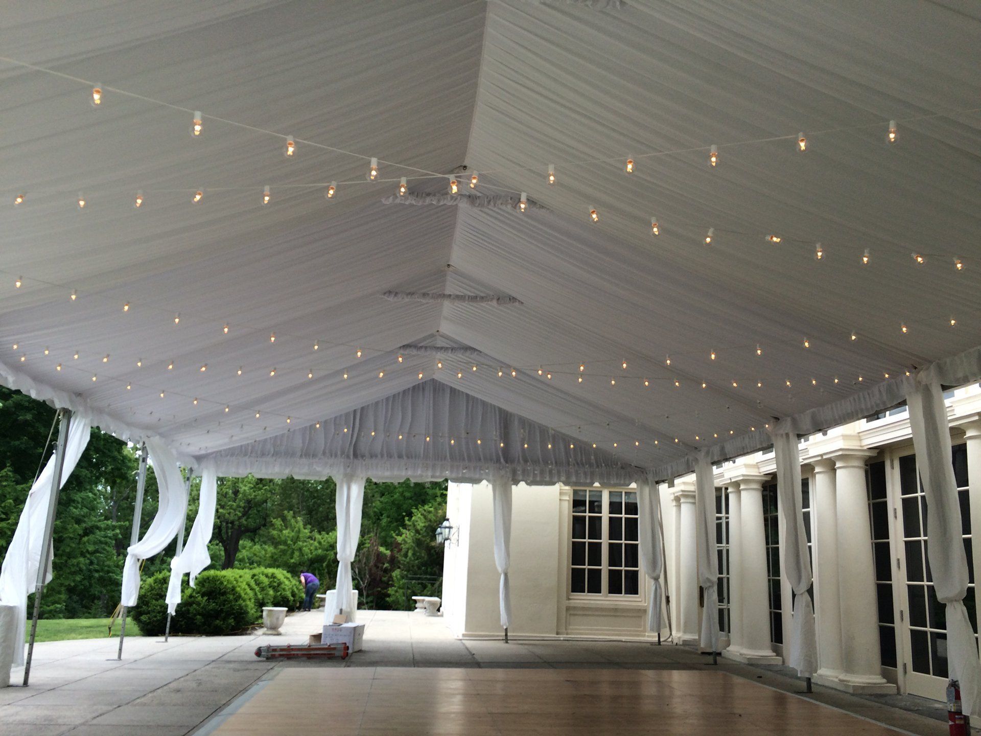White tented event pavilion with string lights, columns, and open sides overlooking greenery