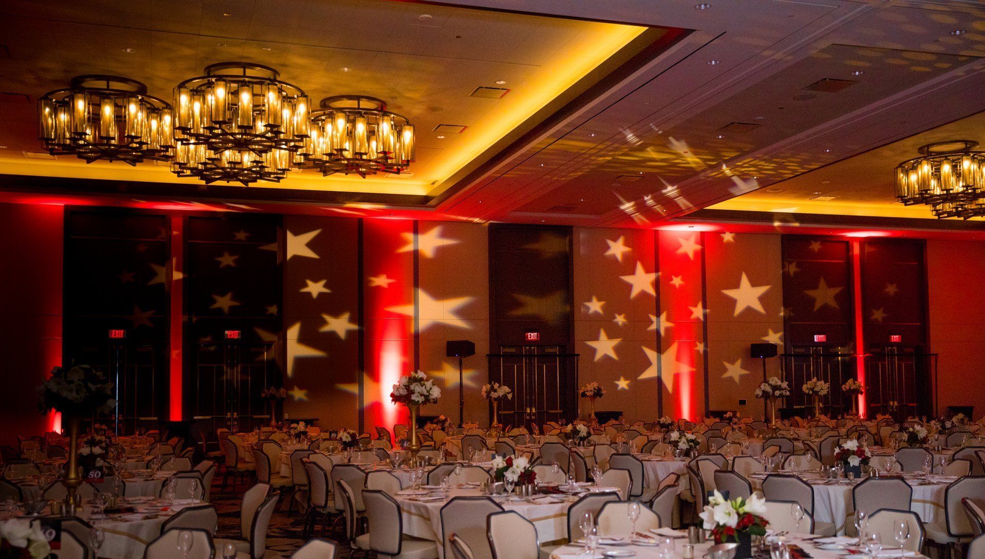 Banquet hall with round tables and red-lit star-patterned stage at a formal event