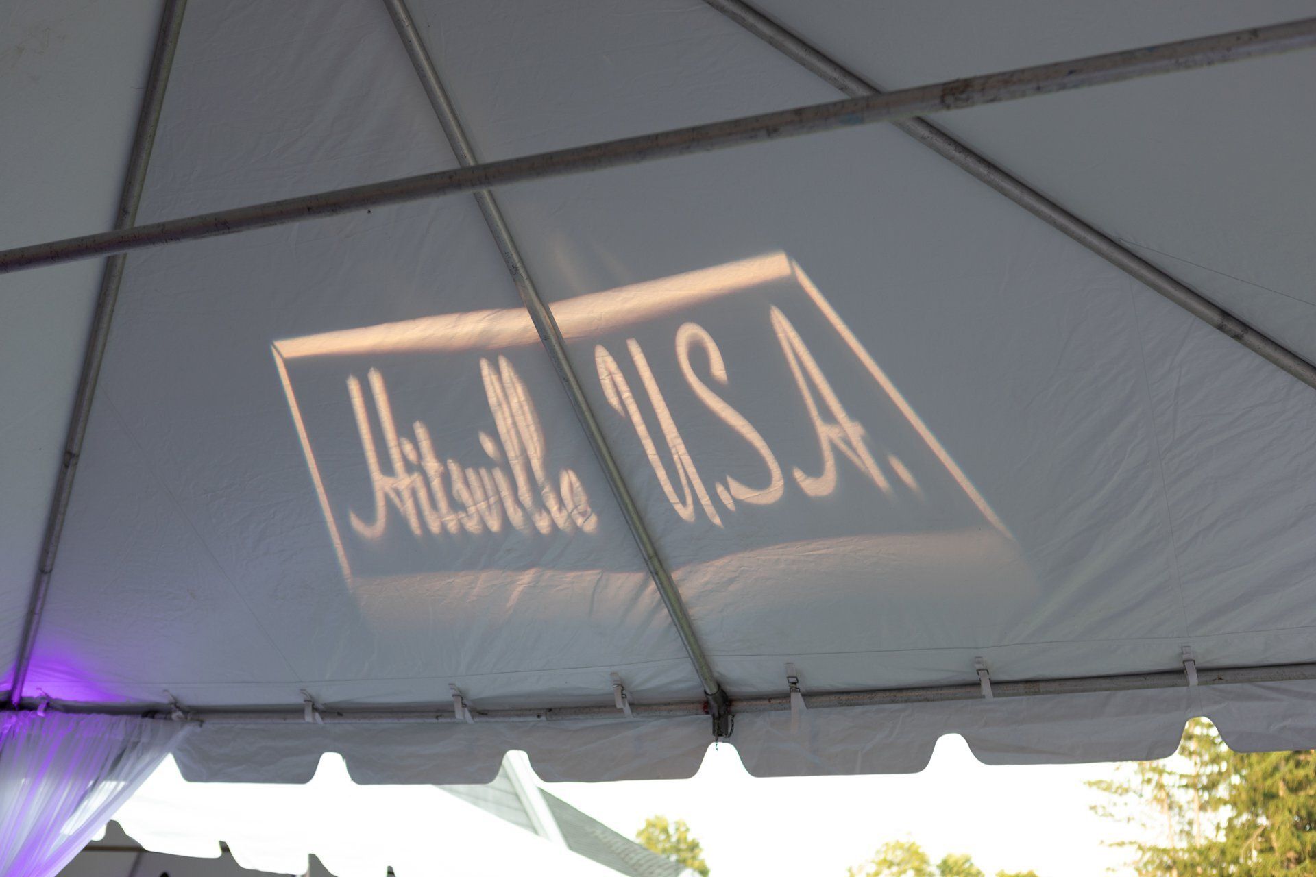 White tent canopy with a projected “United USA” sign and purple light at the edge