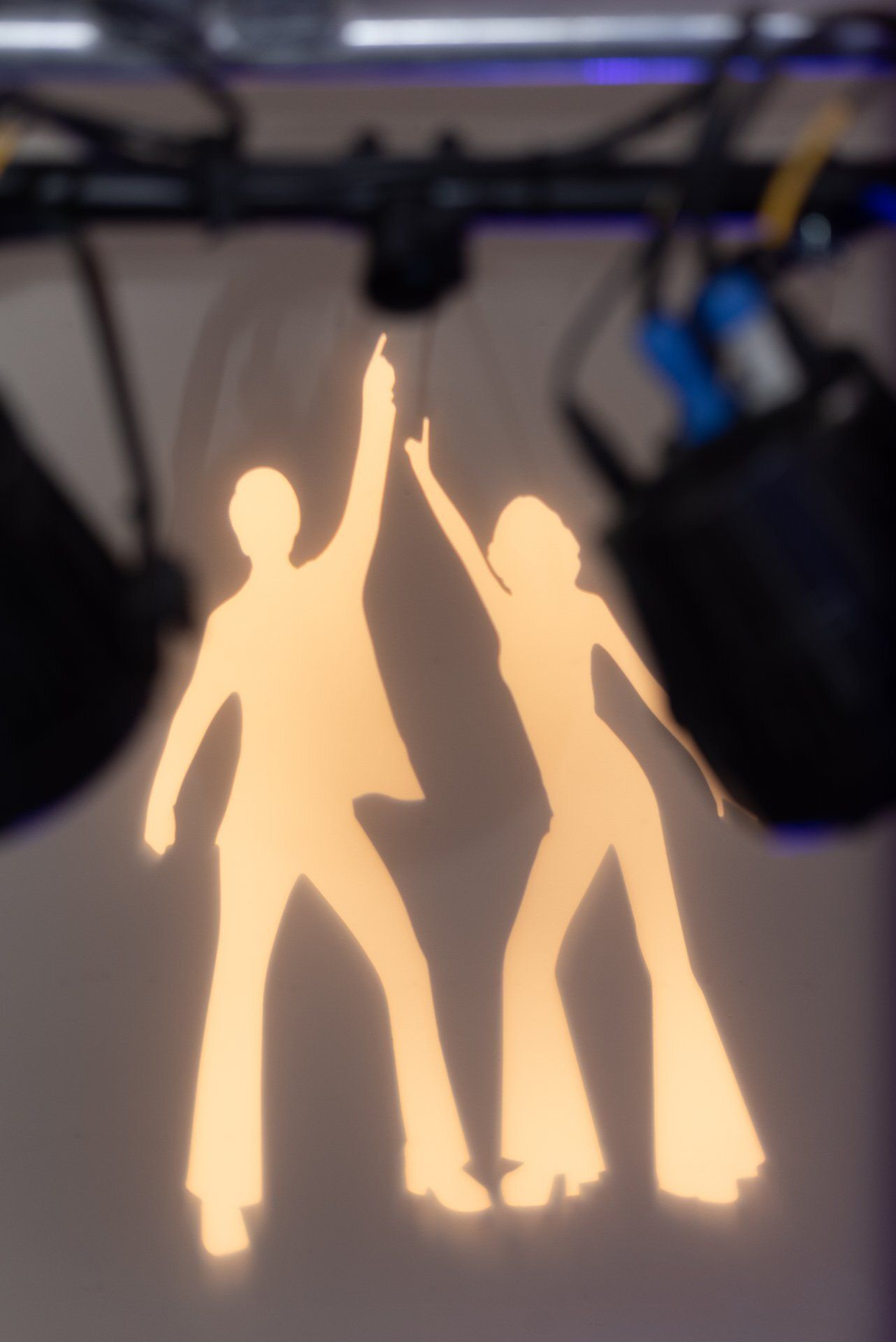 Glowing dancing figures with raised arms, silhouetted against a blurred indoor background.