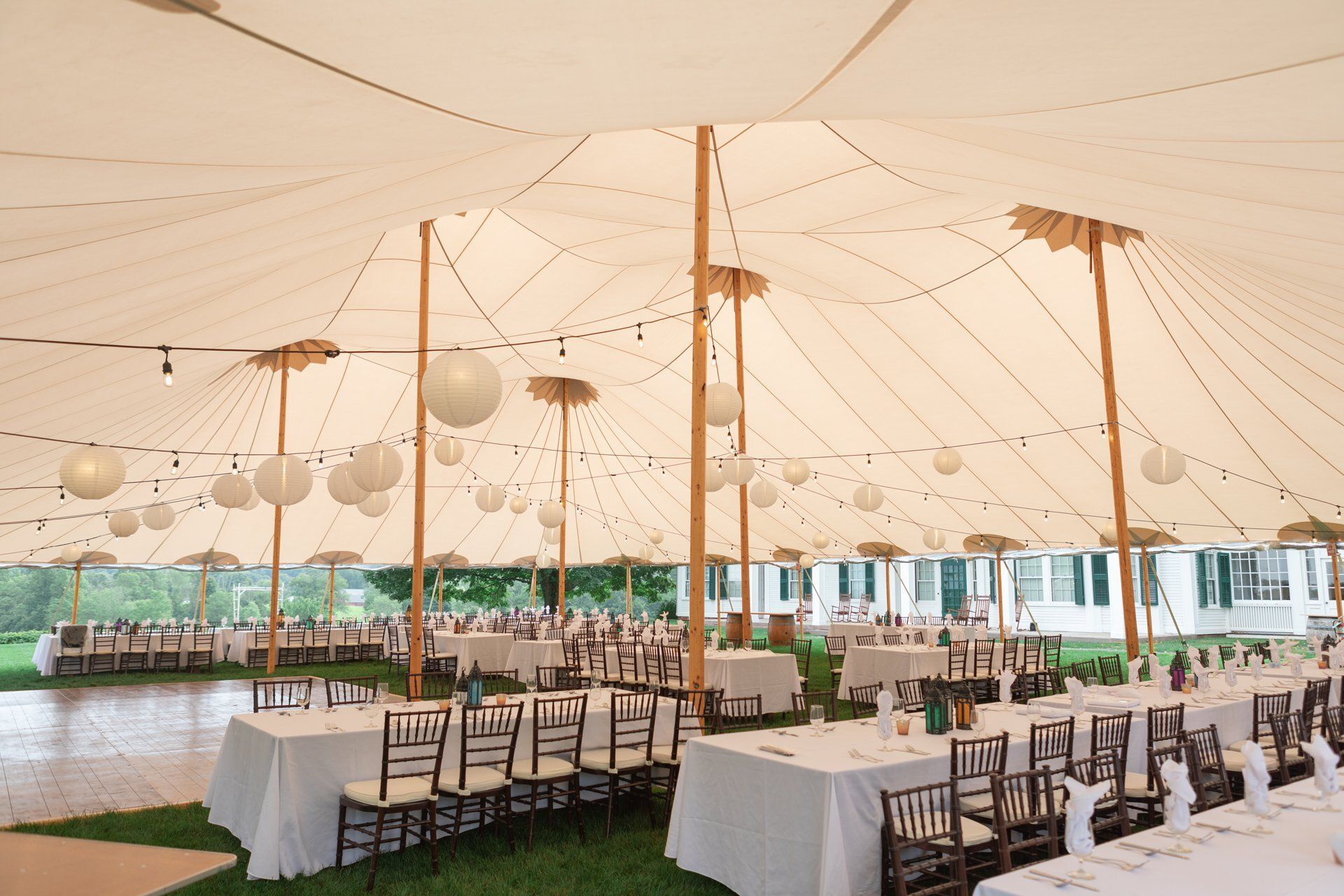 Elegant outdoor event tent with round tables, white linens, and string lights on a grassy lawn