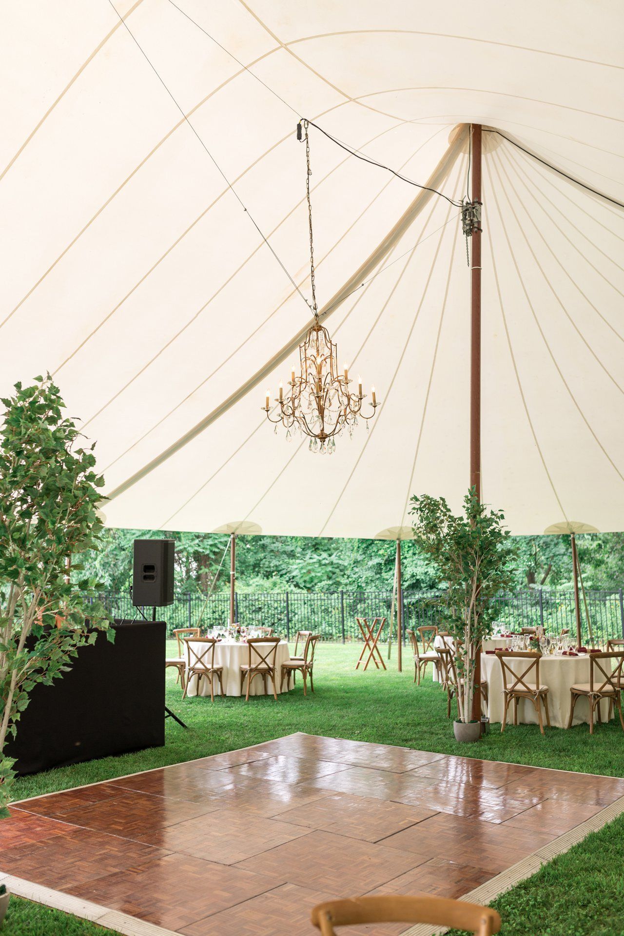 Wedding tent with chandelier, wooden dance floor, string lights, and greenery decor