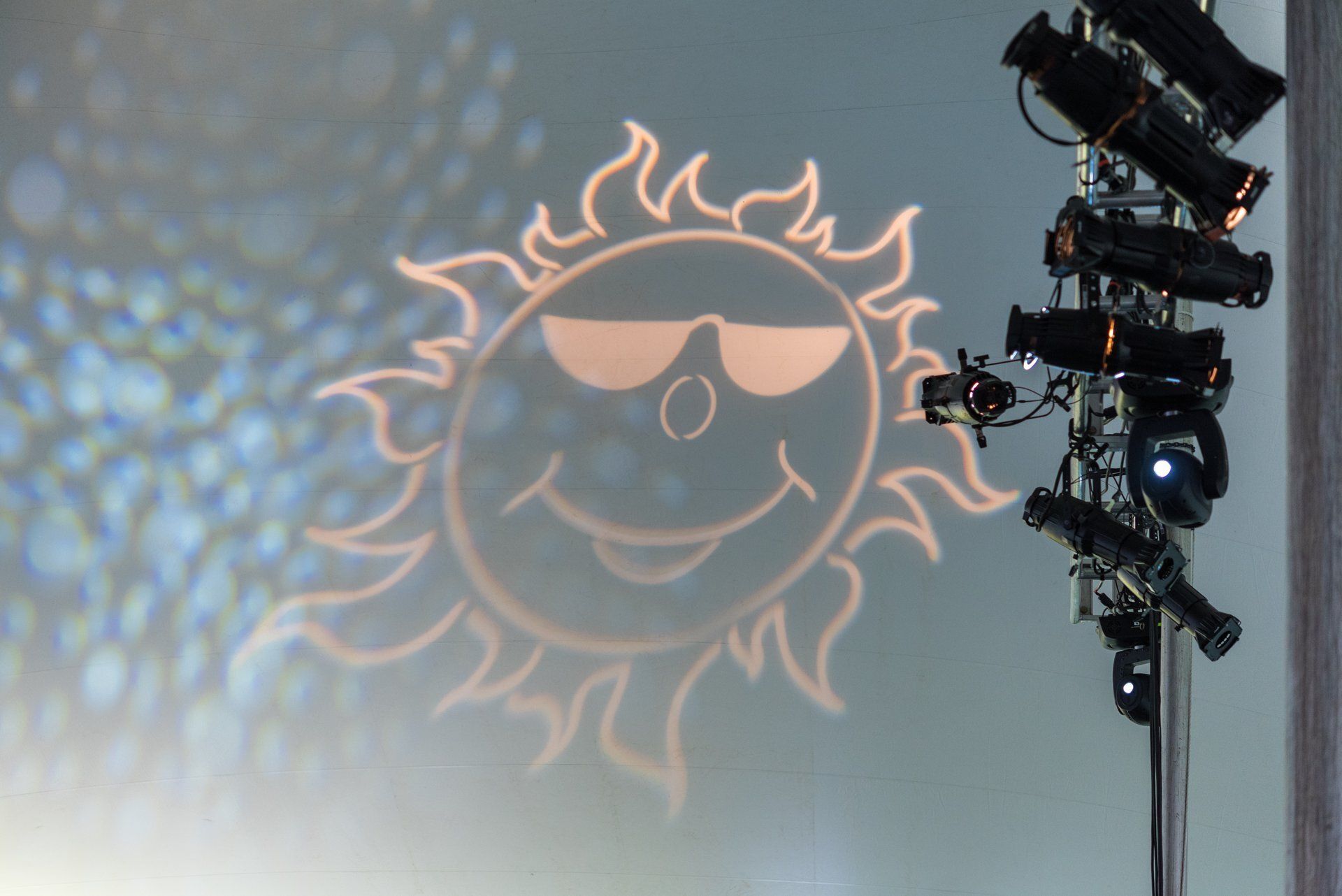 Glowing sun face projection on a wall beside a stage light rig