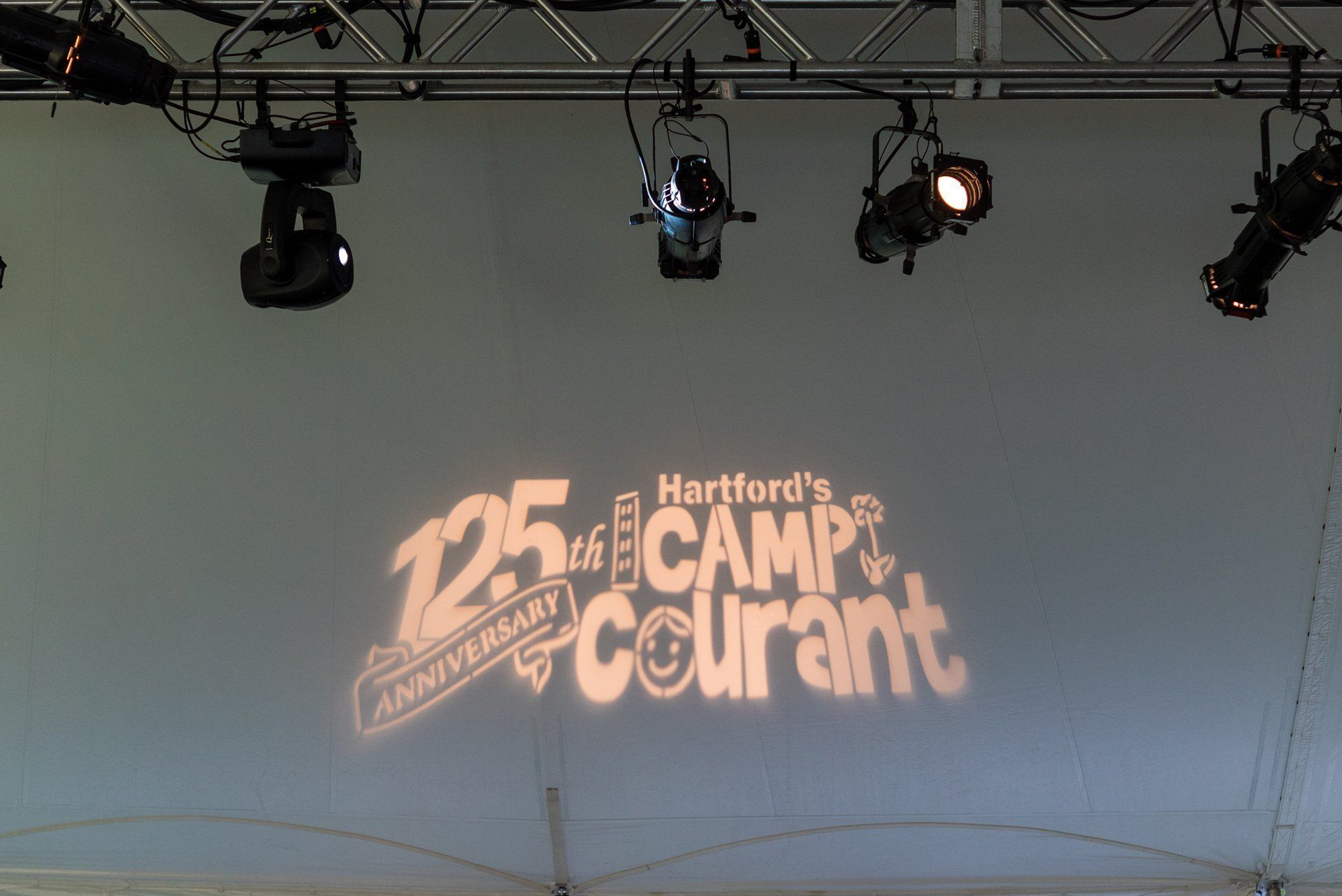 Hartford’s Camp Courant 125th anniversary logo projected on a gray wall under stage lights