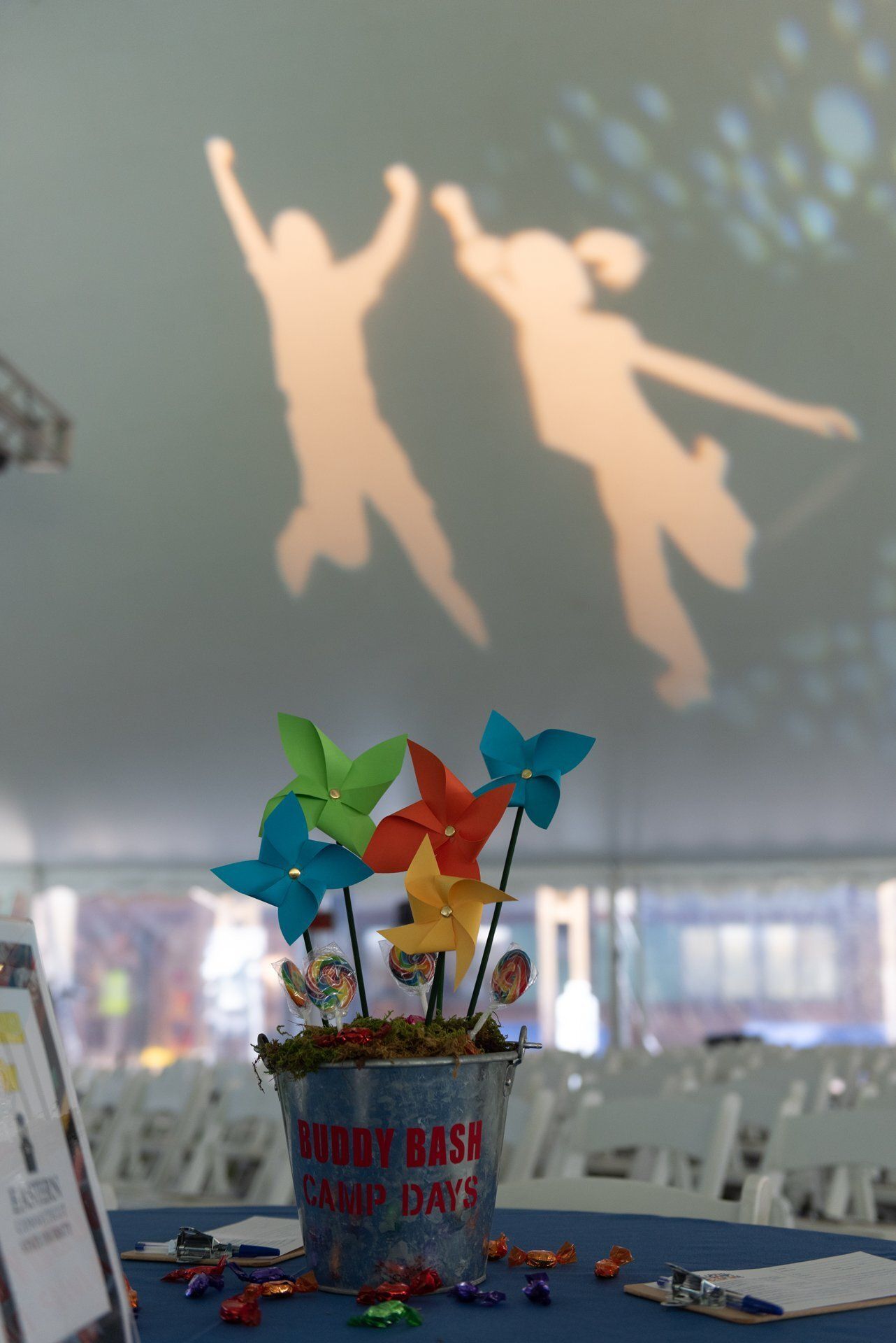 Colorful pinwheels in a cup on a table, with two jumping dancer silhouettes projected on the wall behind.