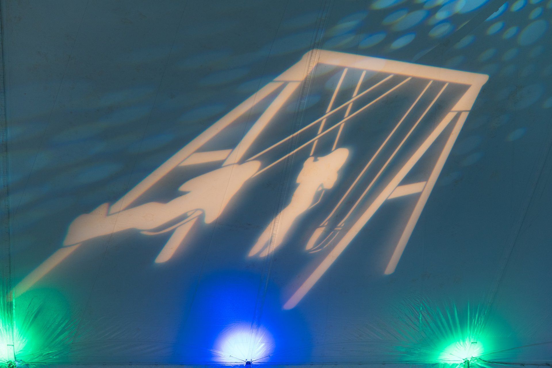 Silhouetted people on a suspended swing frame lit by blue and green stage lights