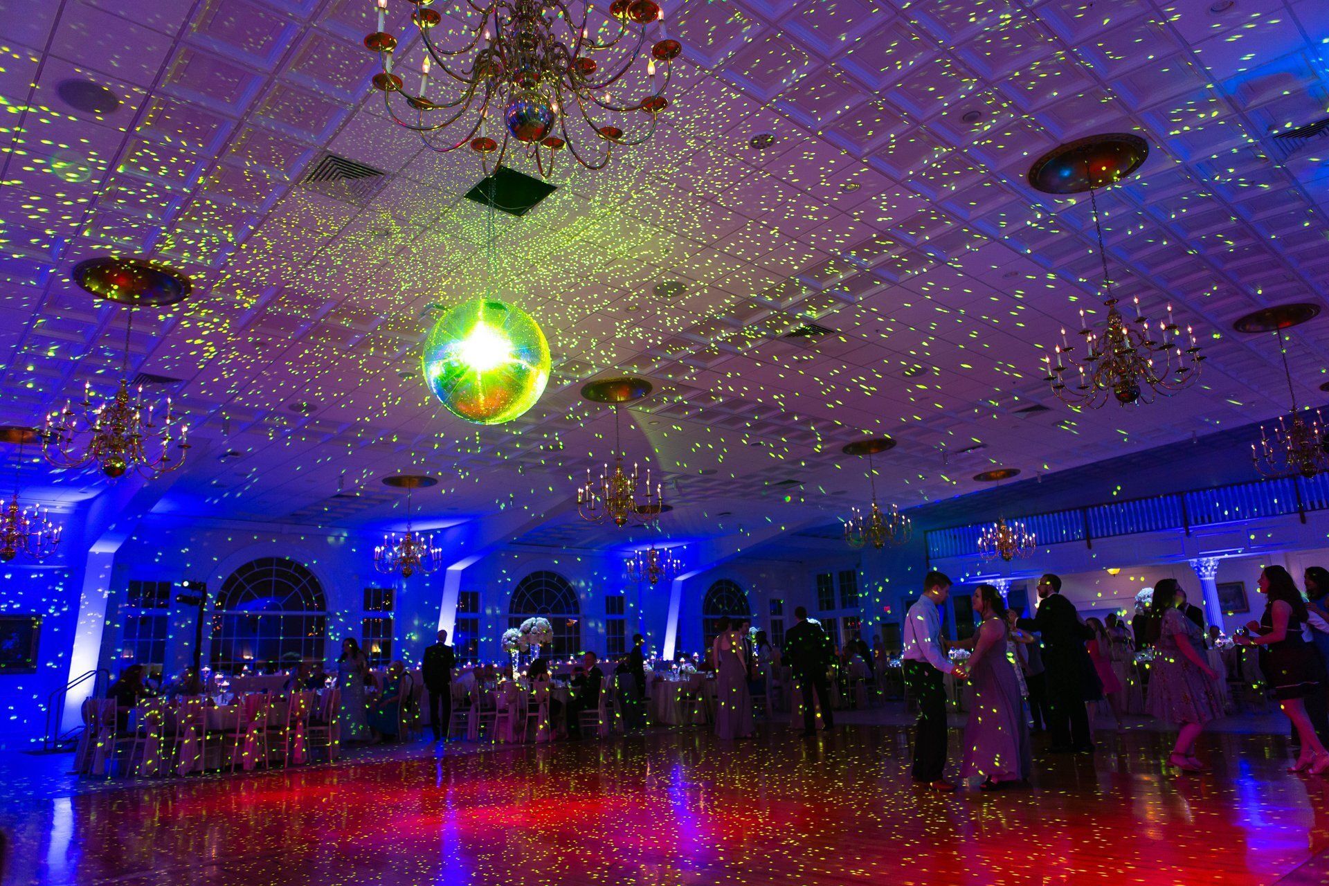 People mingling in a dim banquet hall lit by colorful disco lights and a mirrored ball.