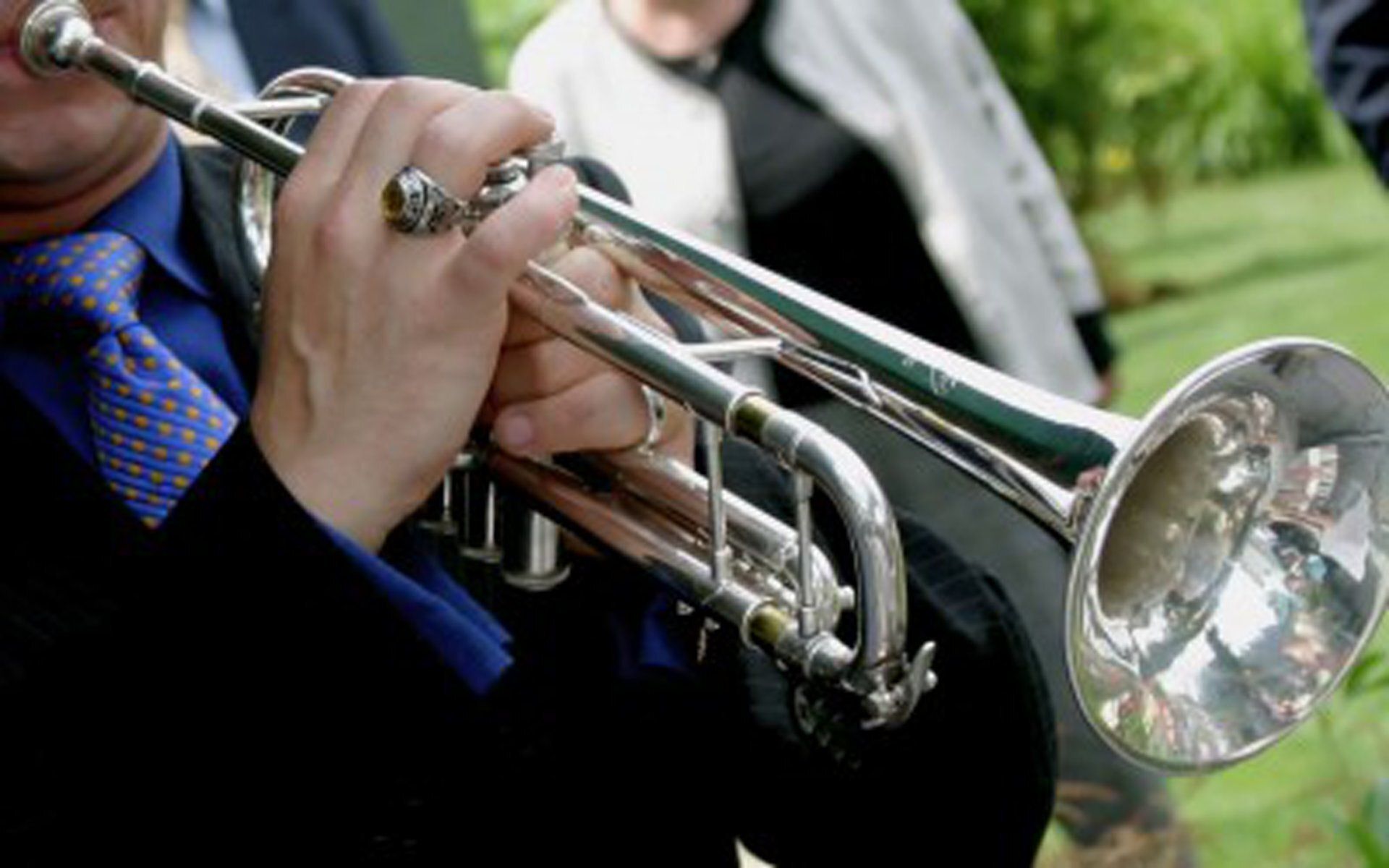 Close-up of hands playing a silver trumpet outdoors, with a blurred green background