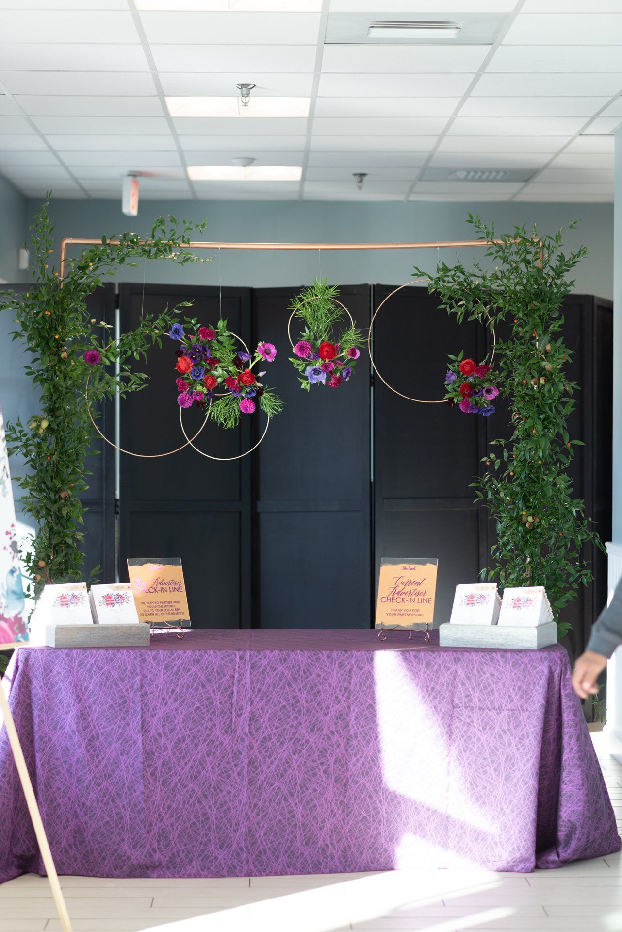 Purple-covered table with floral hoop decorations and small display items in a lobby or booth area