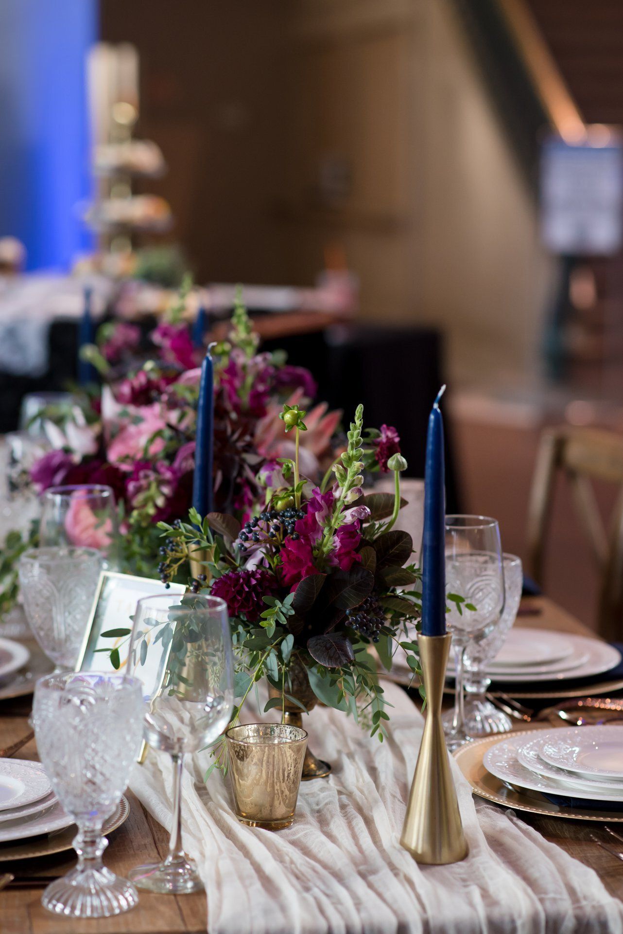 Elegantly set dining table with white plates, blue candles, and a purple floral centerpiece
