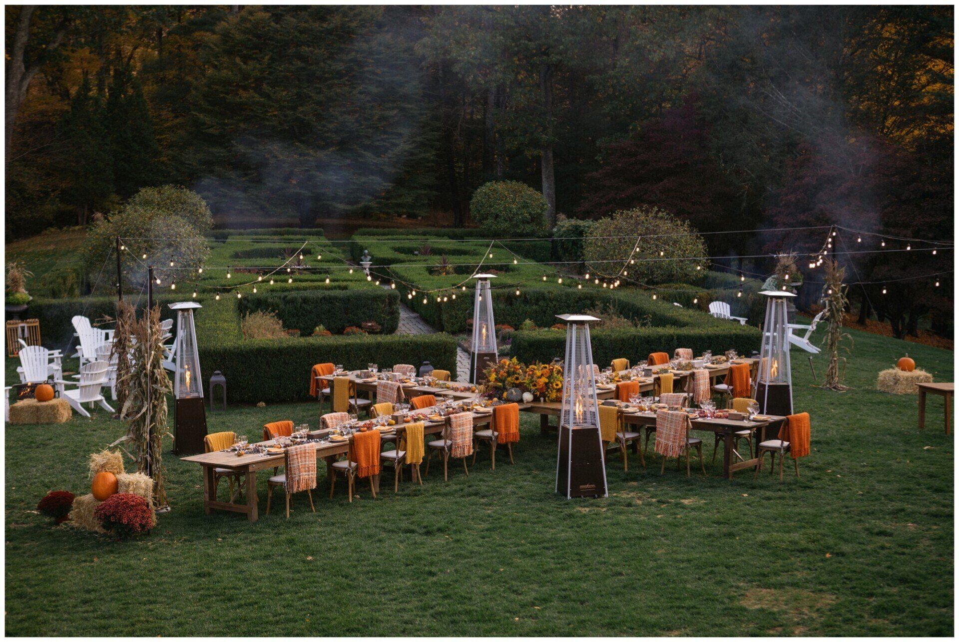 Outdoor formal dining setup on a lawn with orange pumpkins and tall torches at dusk