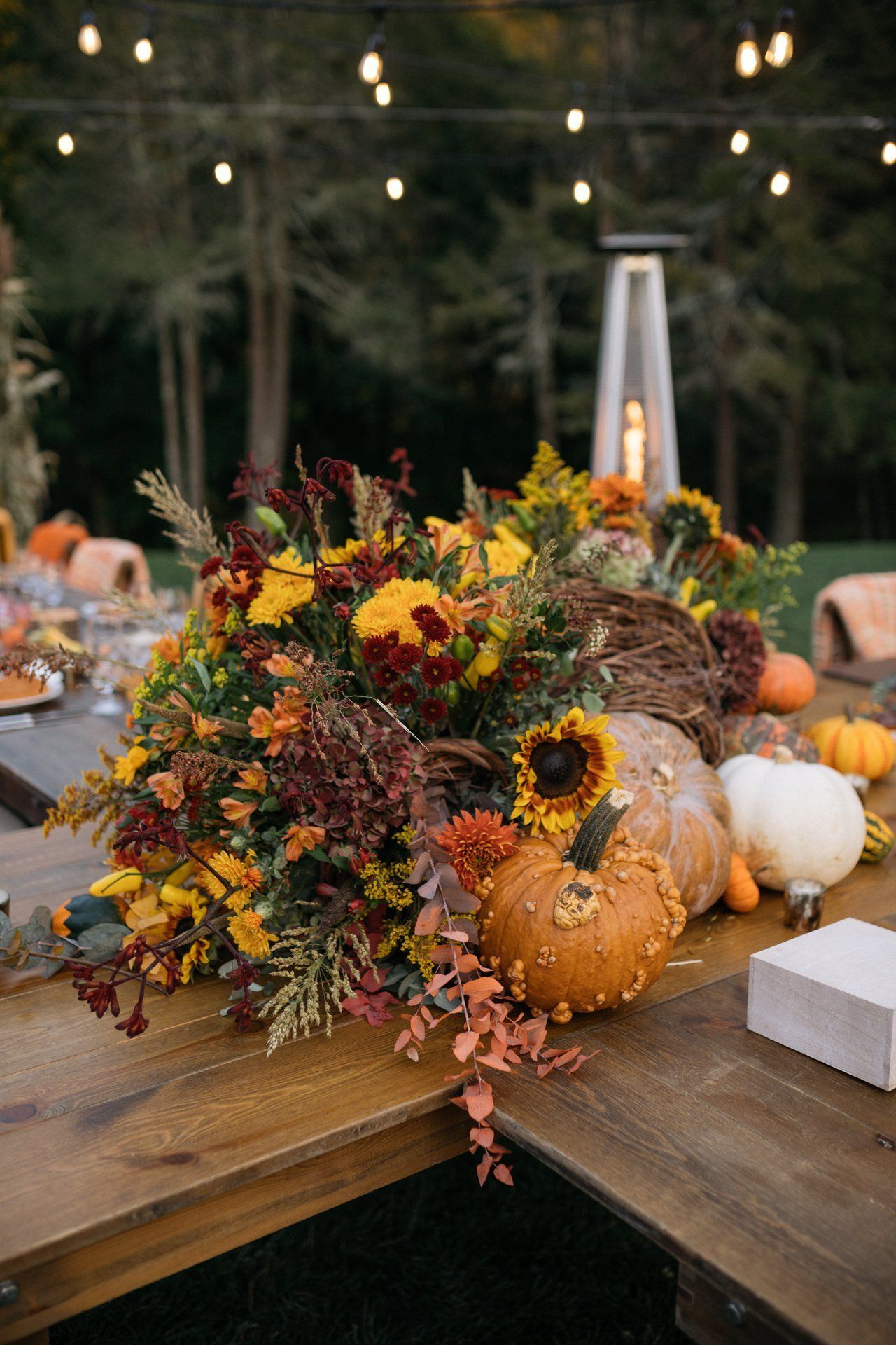 Autumn table centerpiece with pumpkins, sunflowers, and fall foliage outdoors at a dinner setup