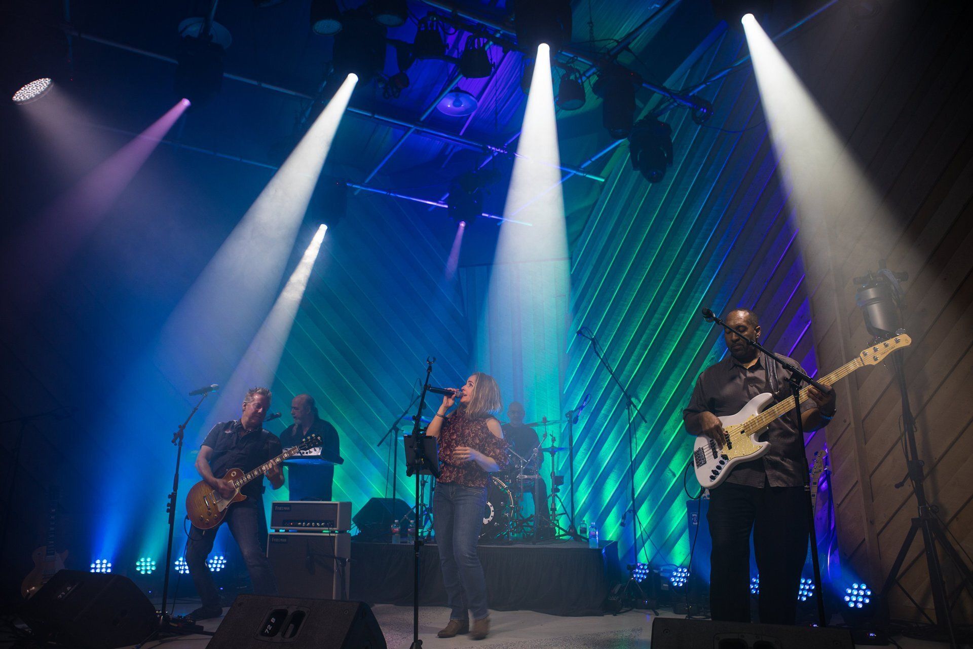 Band performing onstage under blue and purple spotlights with guitars and drums
