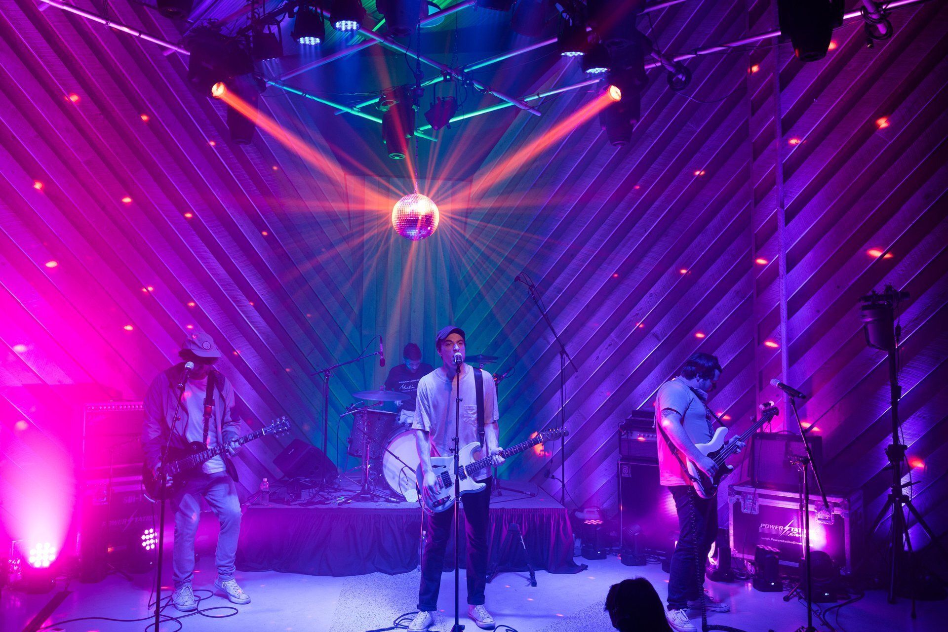 Live band performing onstage under purple and pink lights with a disco ball overhead