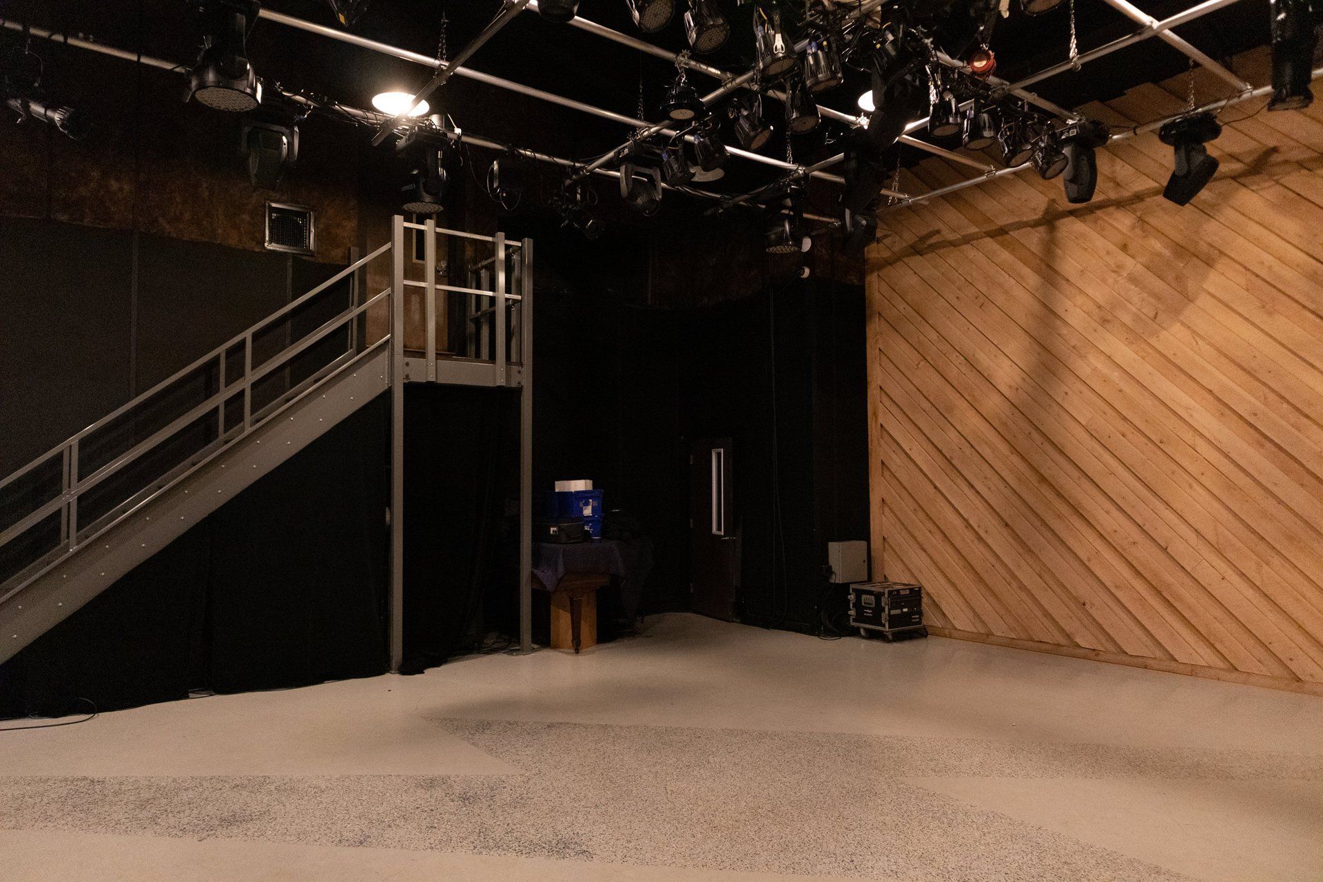 Empty studio set with a staircase, black backdrop, overhead lights, and a wood-paneled wall
