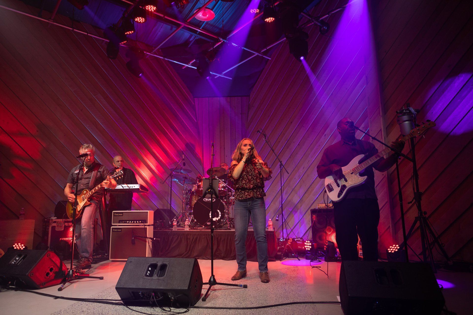 Live band performing on stage under red and purple lights, with microphones, guitars, and drums.