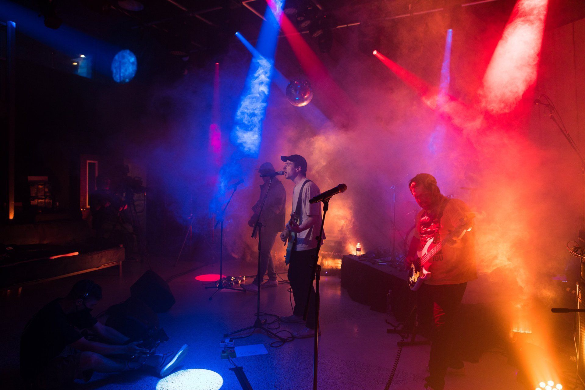 Live rock band performing on smoky stage with red, blue, and orange lights