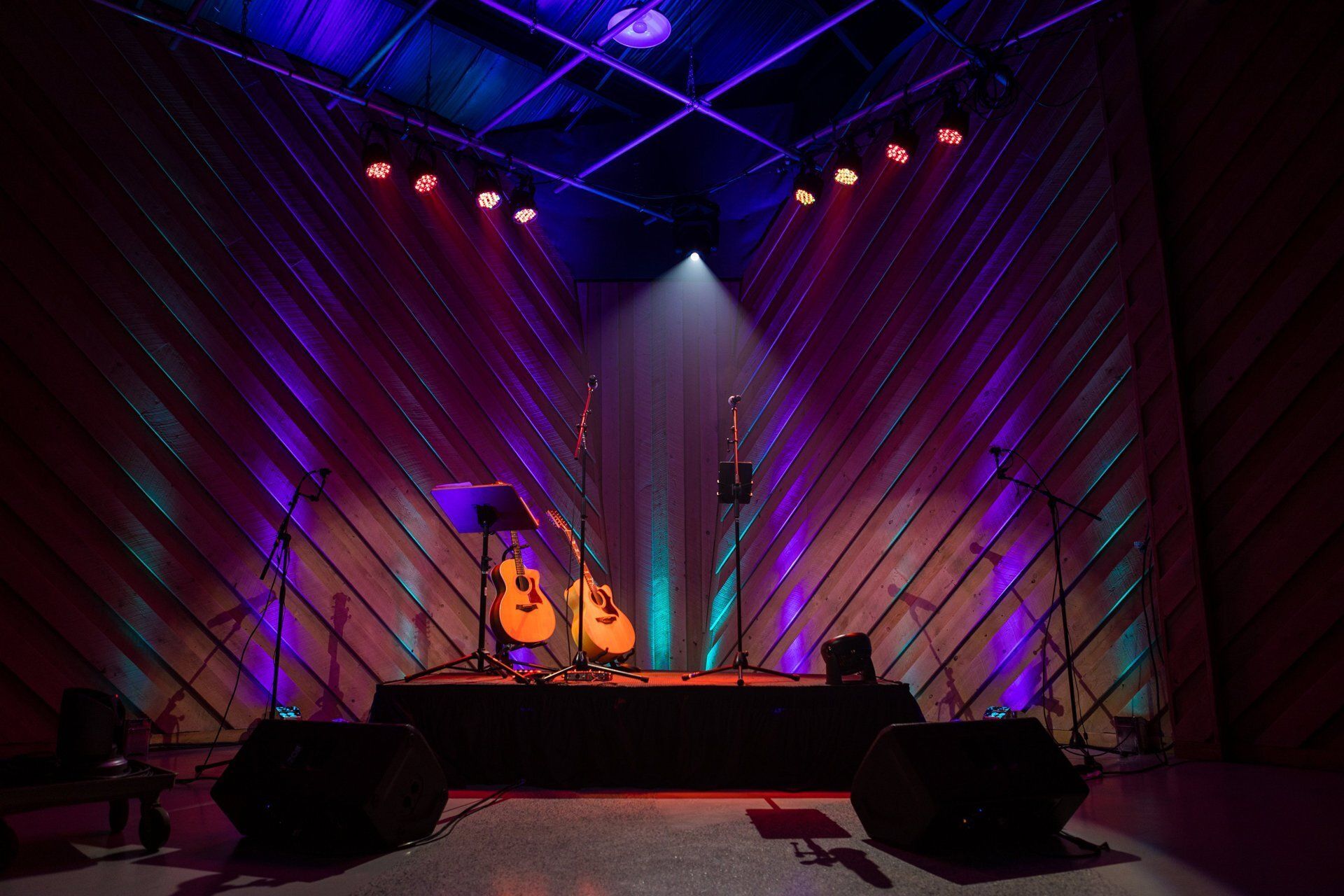 Concert stage with guitars, DJ setup, and purple-blue lights on a dark backdrop