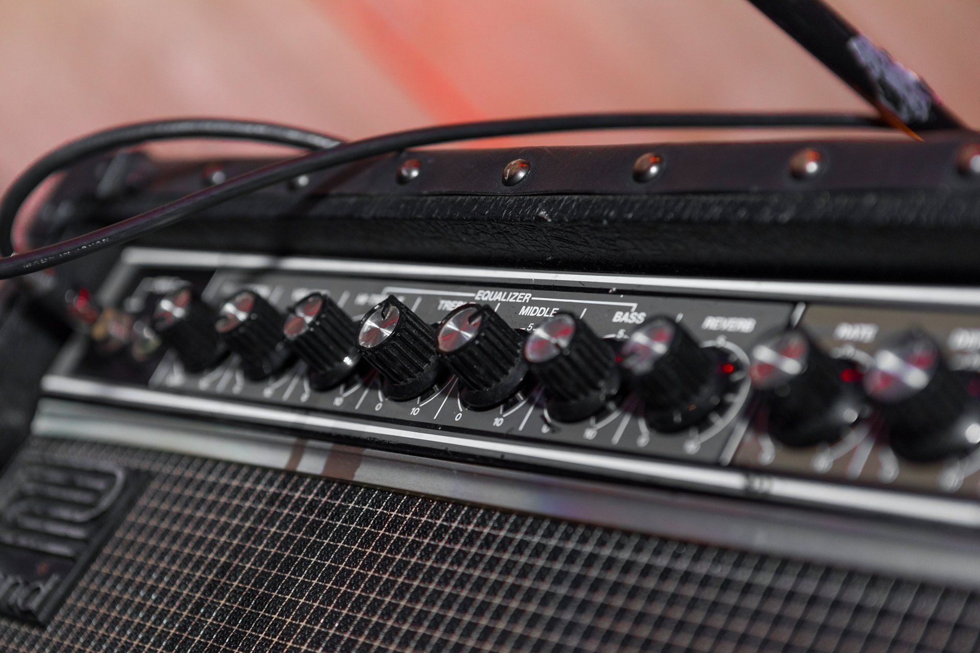 Close-up of a guitar amplifier control panel with black knobs and a metal grille.