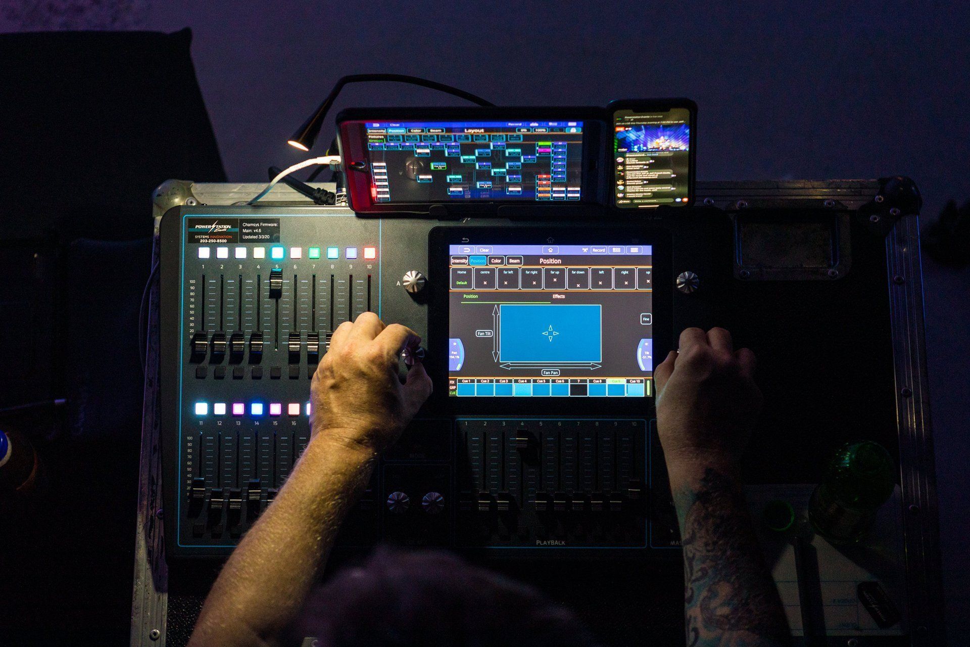 Person operating audio mixing console with multiple screens and illuminated controls in a dark studio