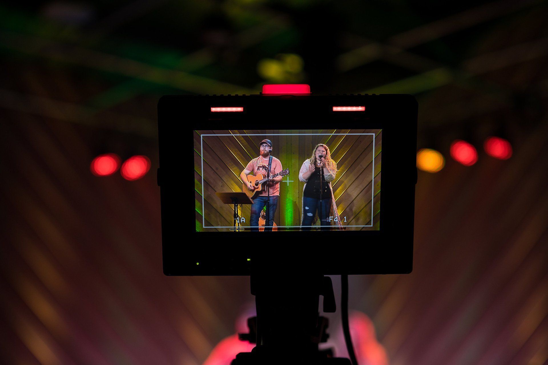 Camera monitor showing two musicians performing on a dimly lit stage