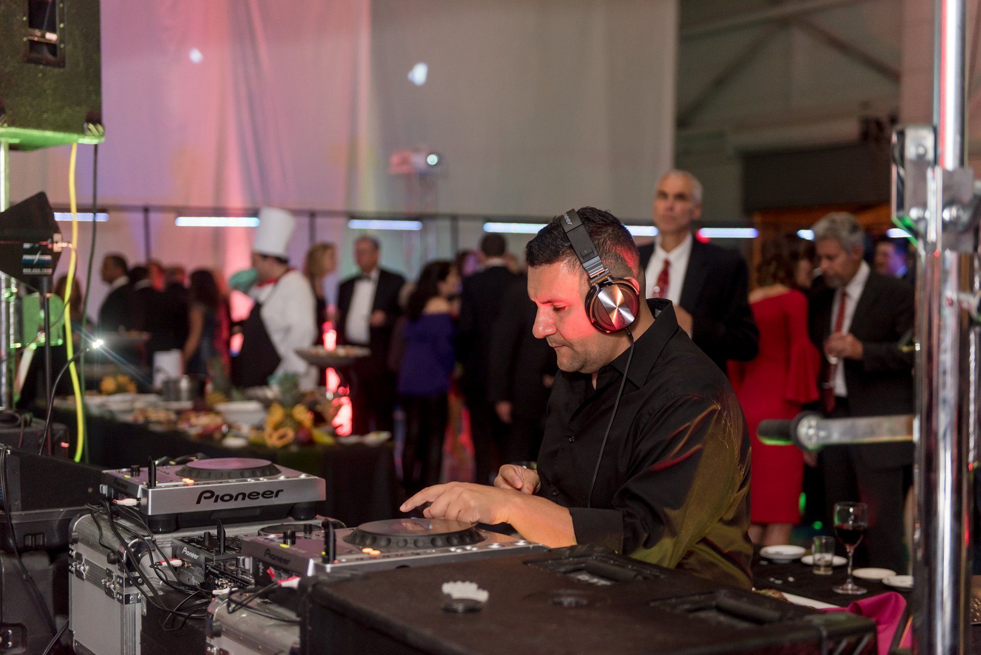 DJ wearing headphones mixing music at a crowded indoor event with colorful lights