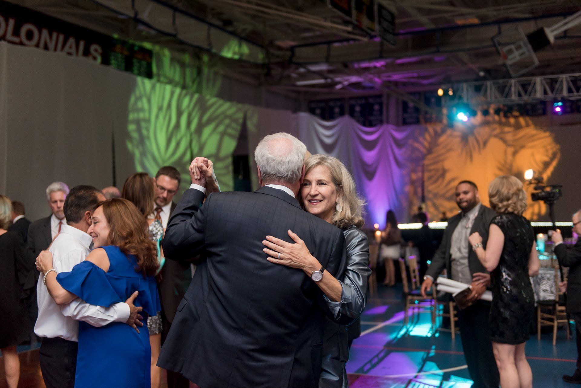 People dancing at a lively indoor event with colorful stage lighting and draped backdrop
