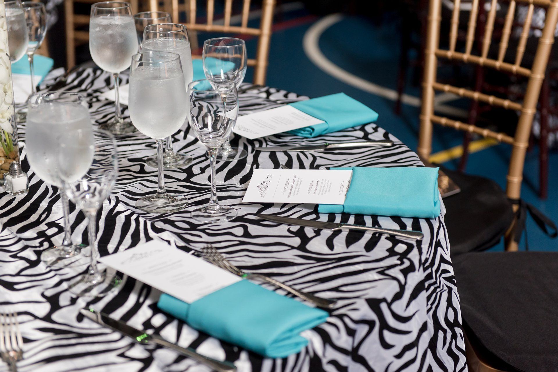 Zebra-print table setting with turquoise napkins, water glasses, and place cards at a formal event