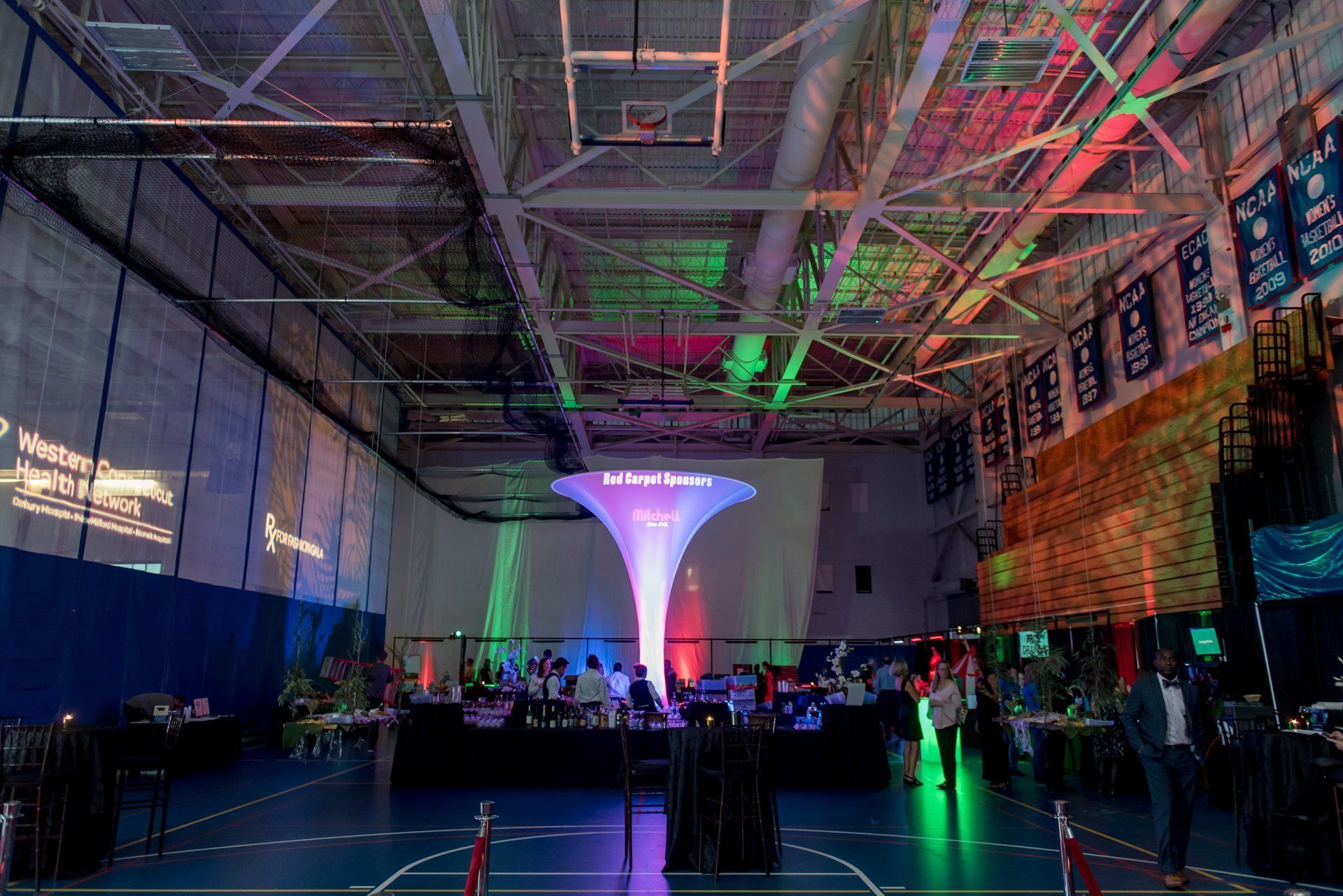 Indoor event space with a glowing purple-and-blue central sculpture and colorful lights over a crowd.