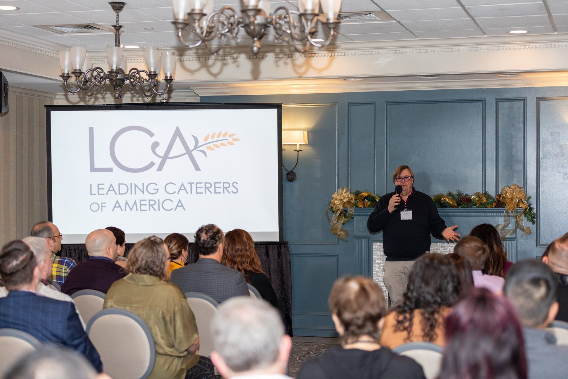 Speaker at podium addresses seated audience at a LOA conference in a chandelier-lit room.