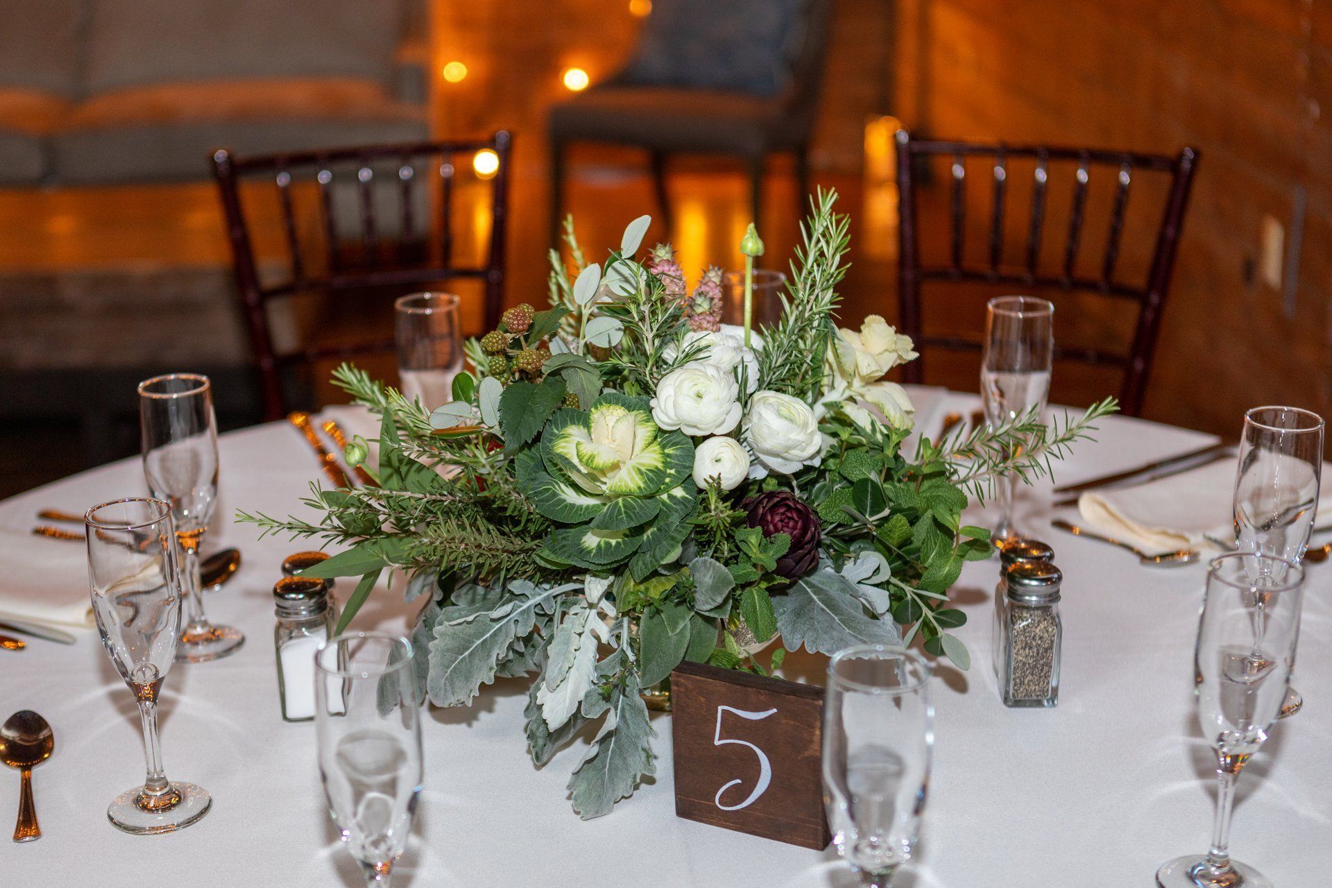 Wedding reception table with white floral centerpiece, greenery, candles, and table number 5