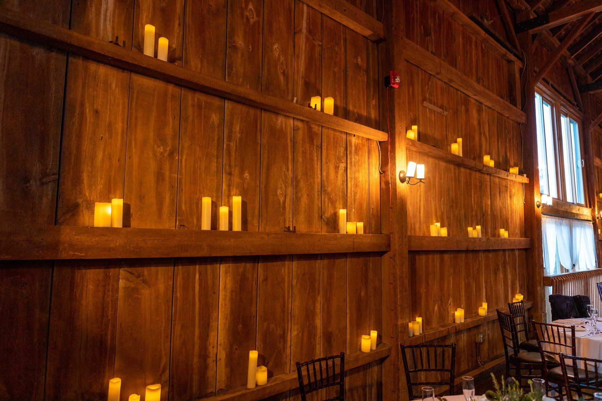 Candlelit wooden interior wall with rows of glowing candles and a table by a window