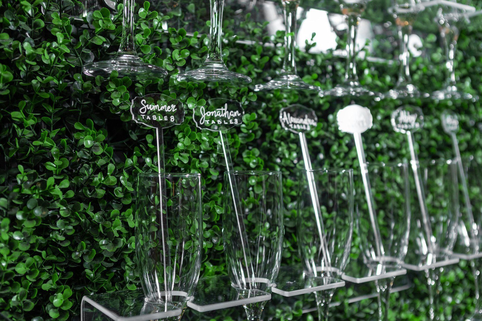 Upside-down wine glasses hanging against a green leafy wall backdrop