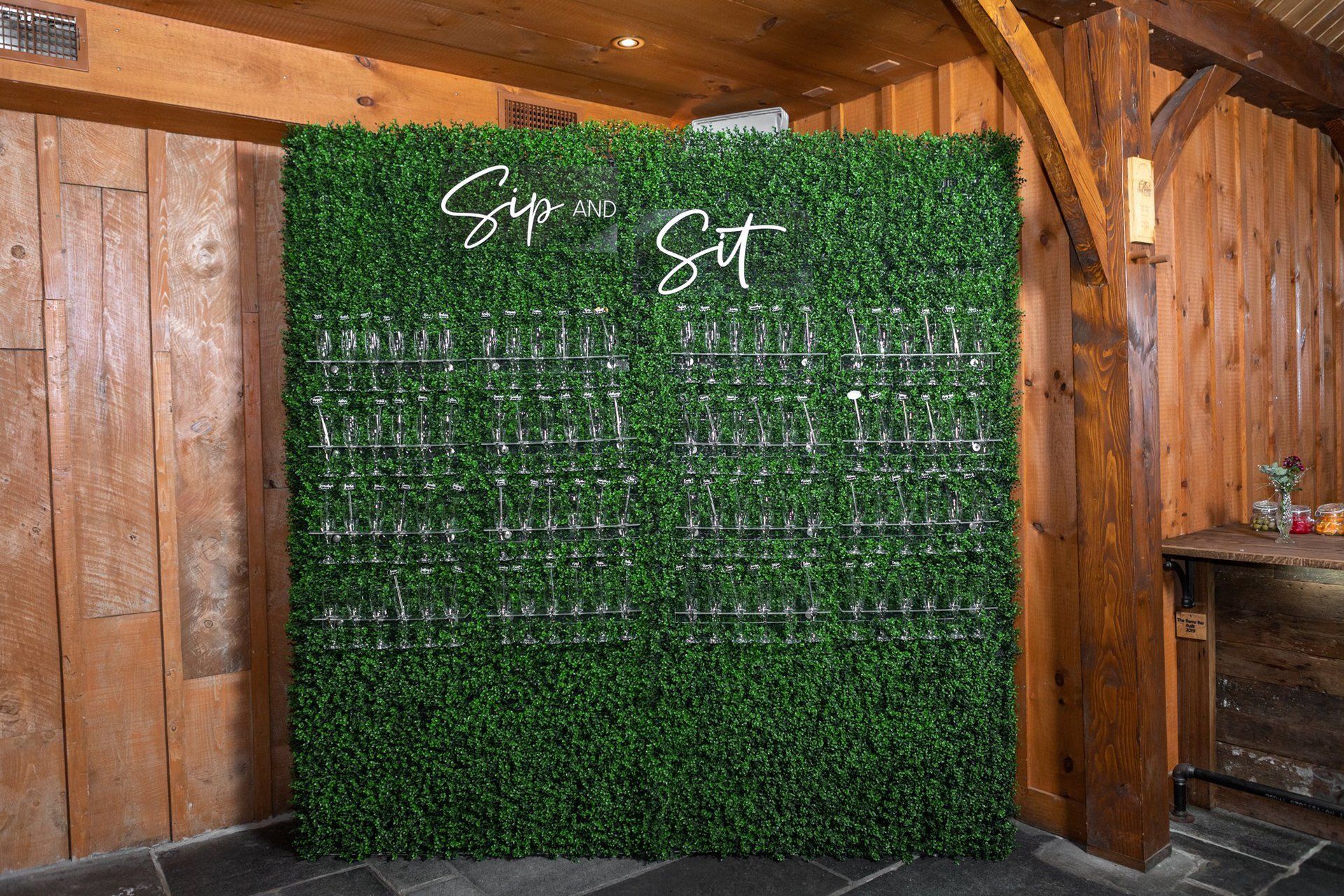 Green faux hedge photo backdrop with white script initials in a rustic wooden room