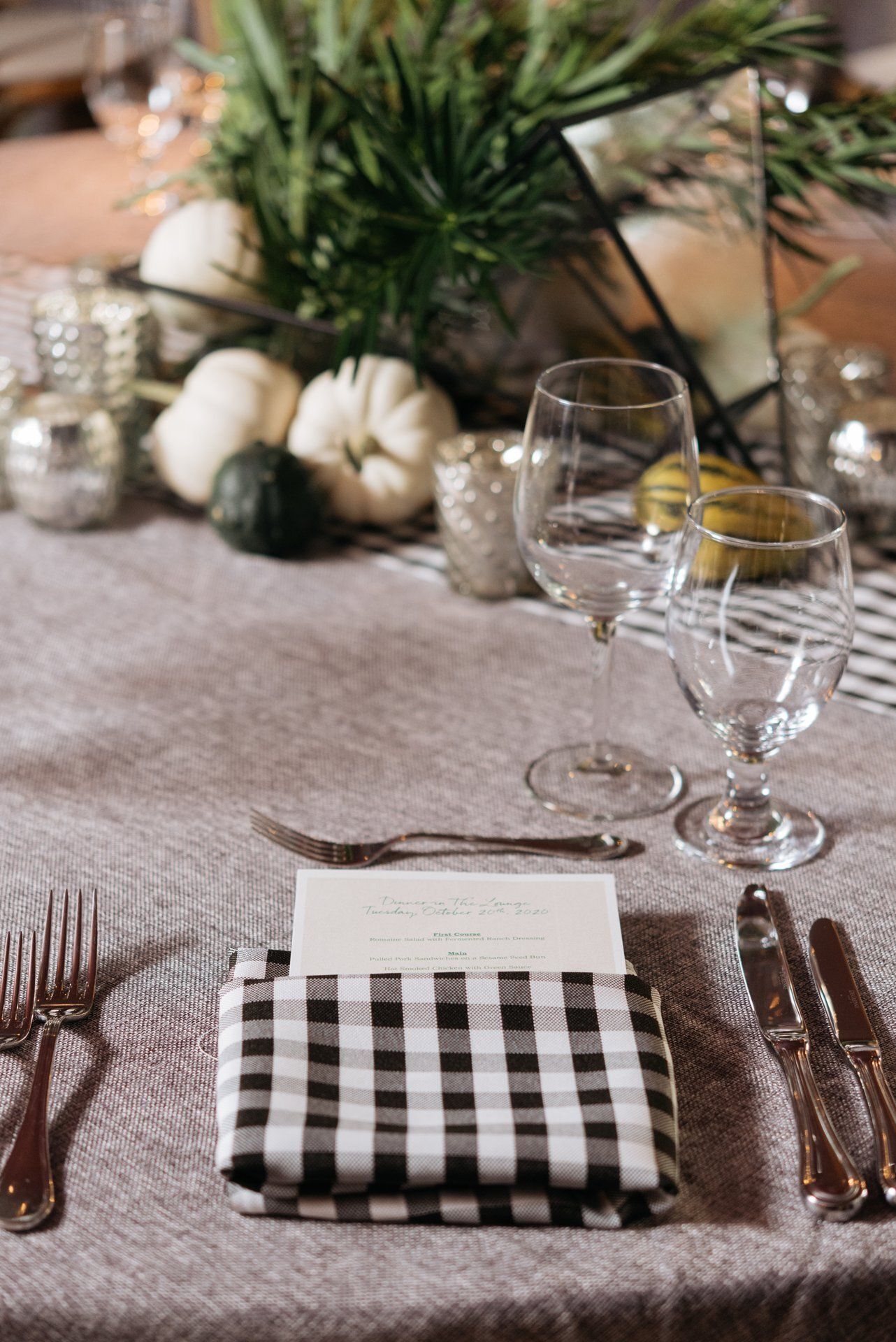 Fall table setting with plaid napkins, glassware, candles, and pumpkins beside greenery