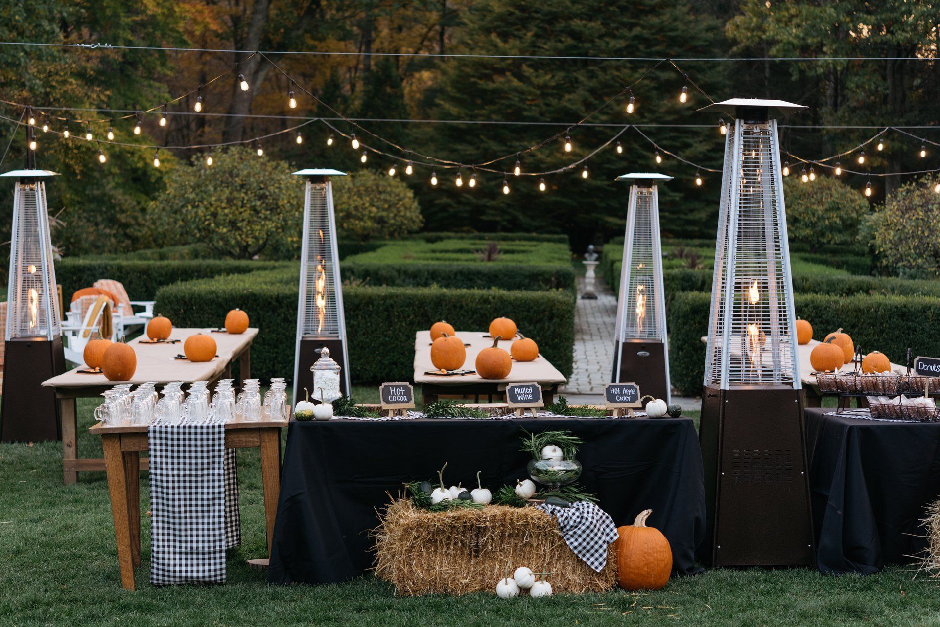 Outdoor dessert buffet with pumpkins, hay bales, and tall patio heaters under string lights