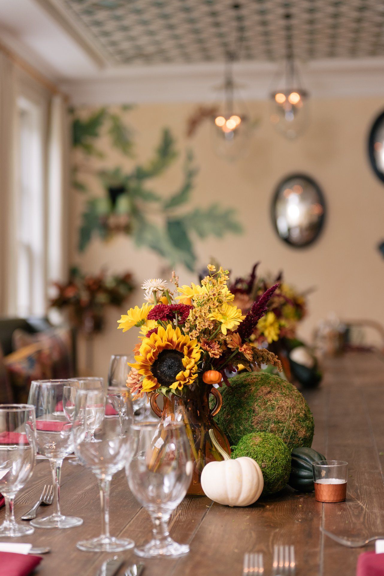 Floral centerpiece with sunflowers and pumpkins on a dining table set with wine glasses in a cozy room