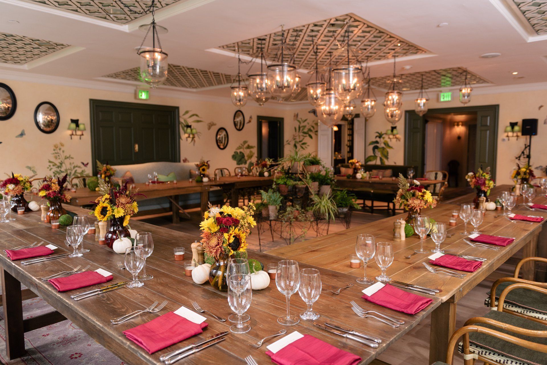 Elegant banquet hall set for a formal dinner with flower centerpieces, red napkins, and chandeliers