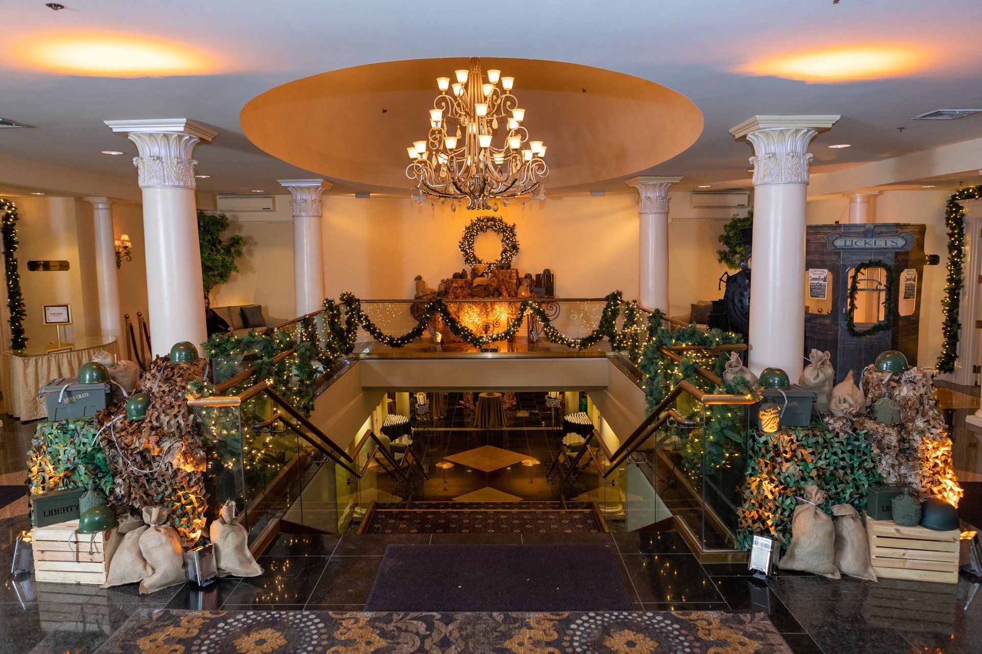 Elegant hotel lobby with chandelier, marble columns, grand staircase, and gold holiday decorations