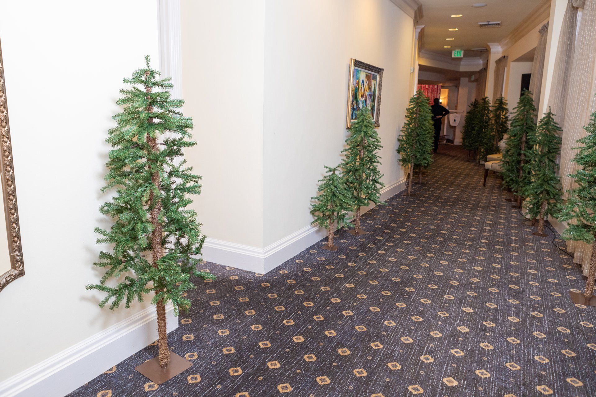 Hotel hallway decorated with small Christmas trees along patterned carpeted corridor
