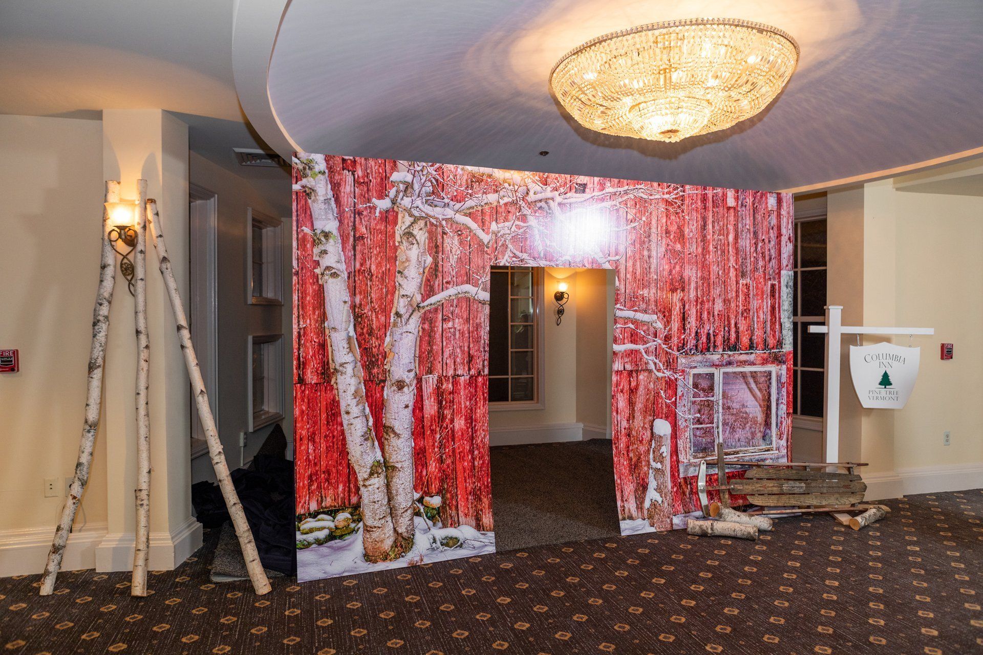 Indoor event entrance decorated with red-and-white birch tree panels and a chandelier overhead