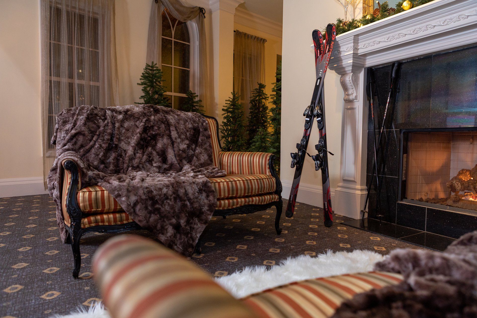 Cozy living room with fur-covered chairs, potted plants, and a lit fireplace