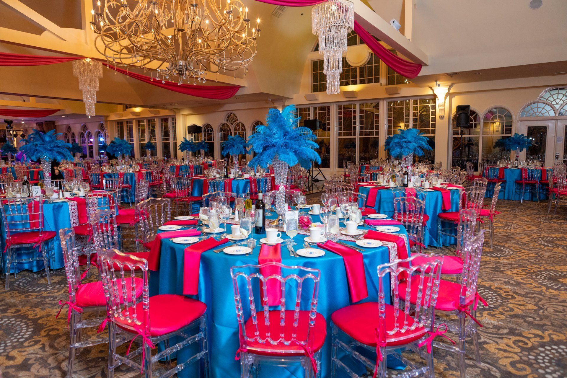 Elegant banquet hall with blue and red table settings and chandeliers, ready for an event