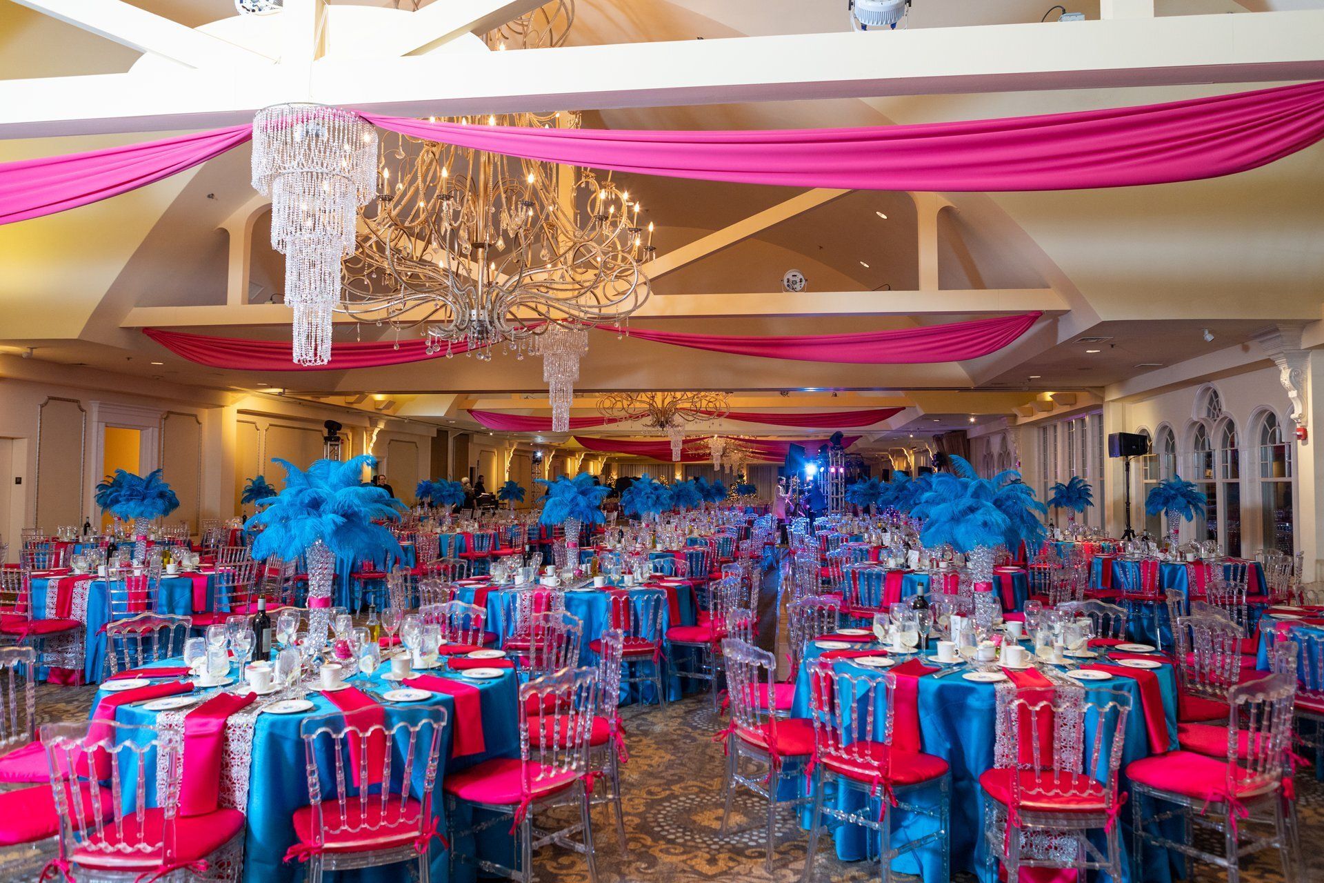 Banquet hall with pink and blue decor, chandeliers, and round tables set for an elegant event
