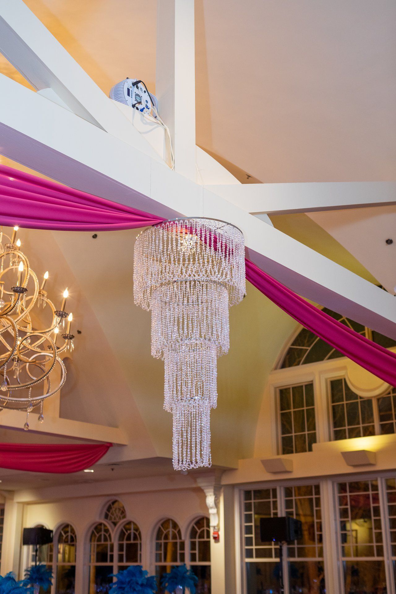 Elegant crystal chandelier with pink drapery and a vaulted ceiling in a banquet hall