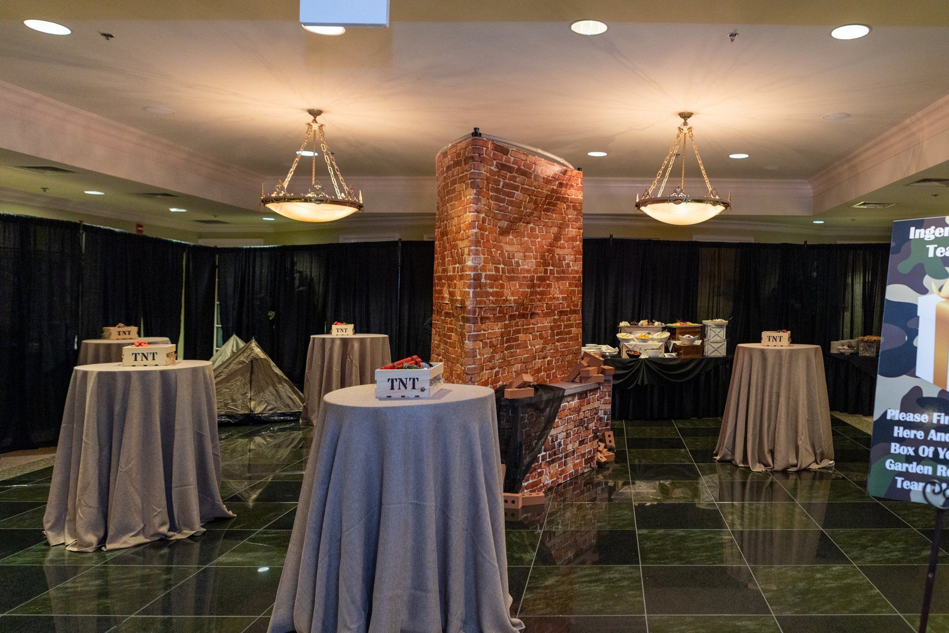 Banquet hall with cocktail tables draped in gray cloth and a stone pillar centerpiece under warm lights