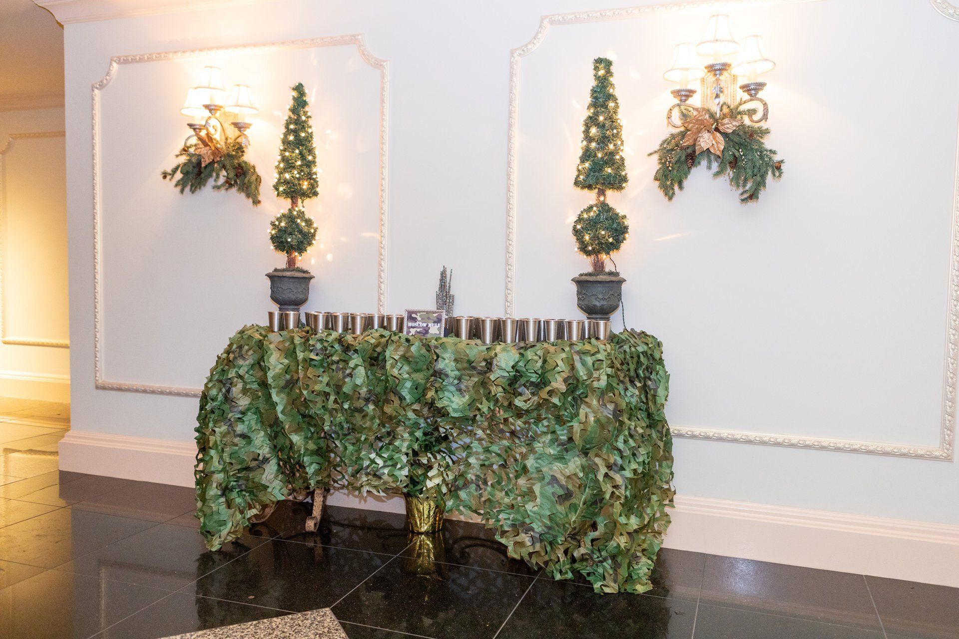 Decorated table with green garland, candles, and potted evergreens in a hallway display